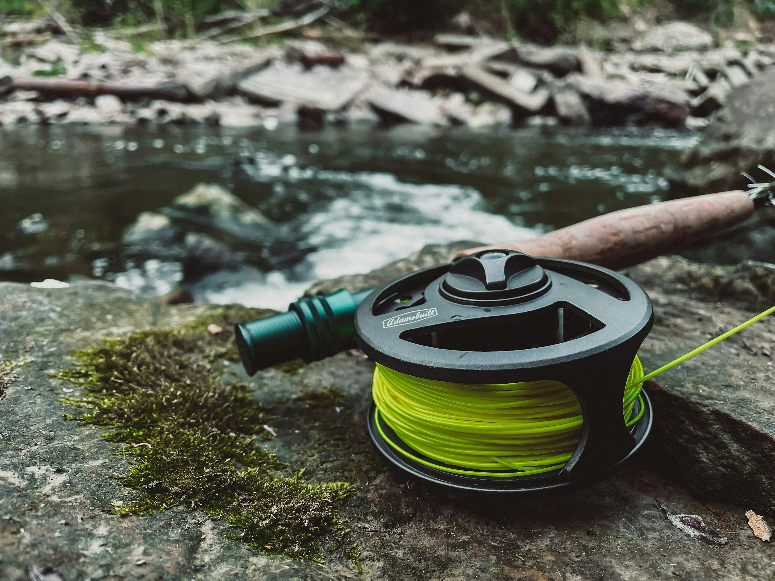 Fly fishing rod and reel resting on moss-covered rocks beside a flowing West Coast river near Lake Brunner.