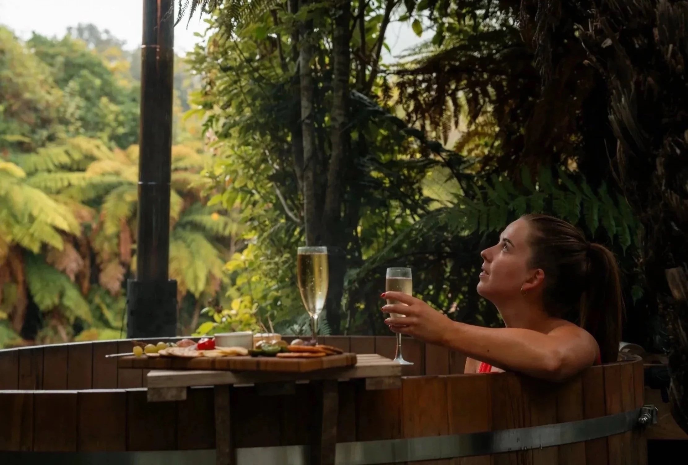Guest relaxing in a private hot tub at Lake Brunner Eco Lodge, enjoying drinks surrounded by native West Coast bush.