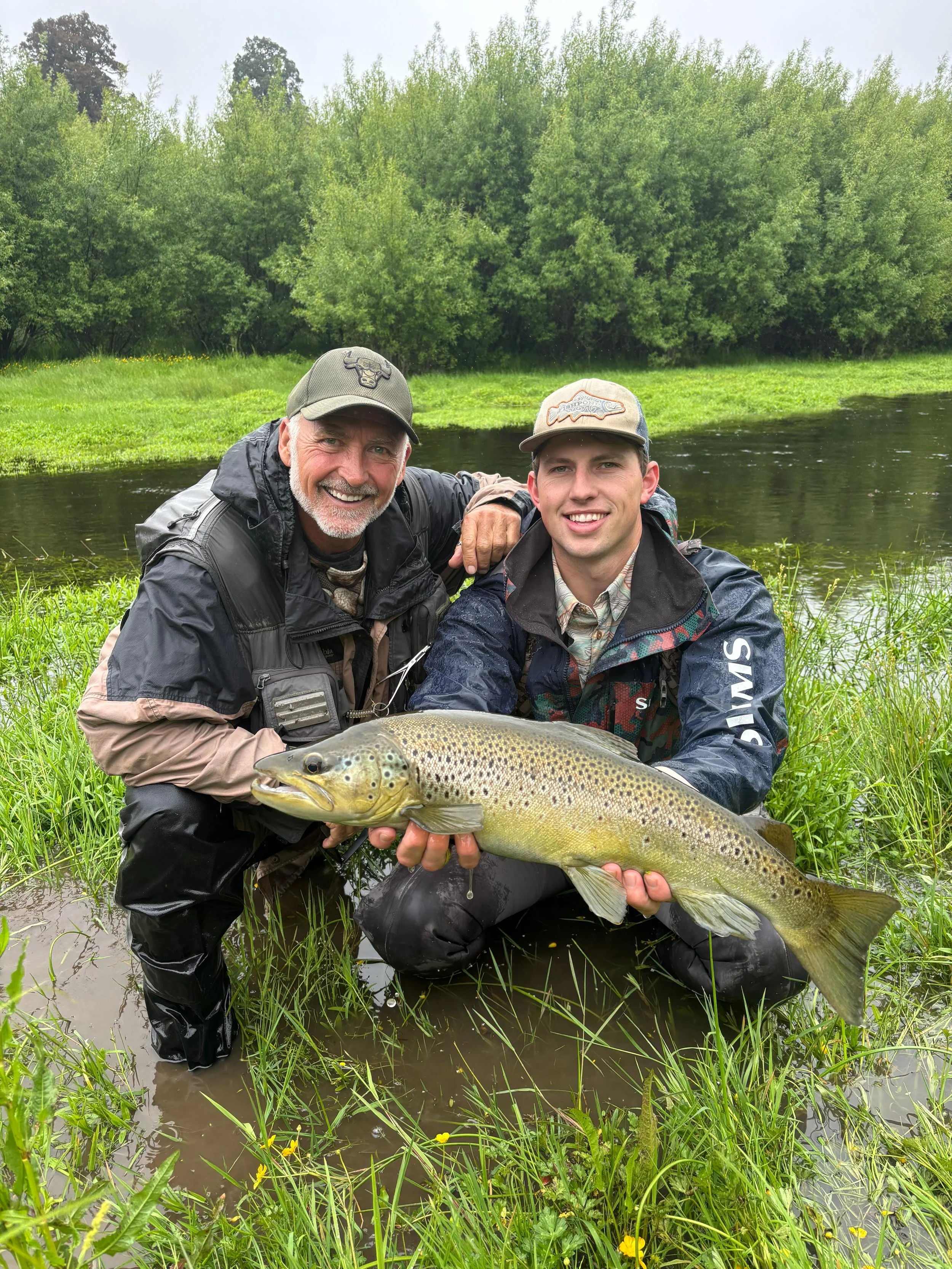 Fly-fishing guide and guest holding a wild brown trout during a guided fishing trip on a West Coast river near Lake Brunner, New Zealand.