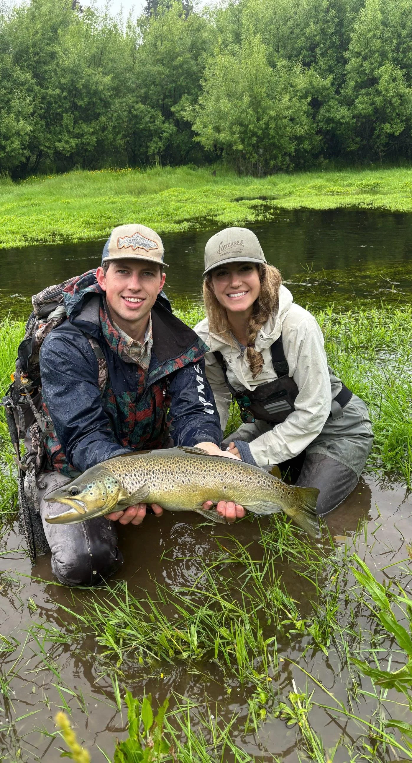 Two anglers holding a wild brown trout during a guided fly-fishing trip on a West Coast river near Lake Brunner, New Zealand.