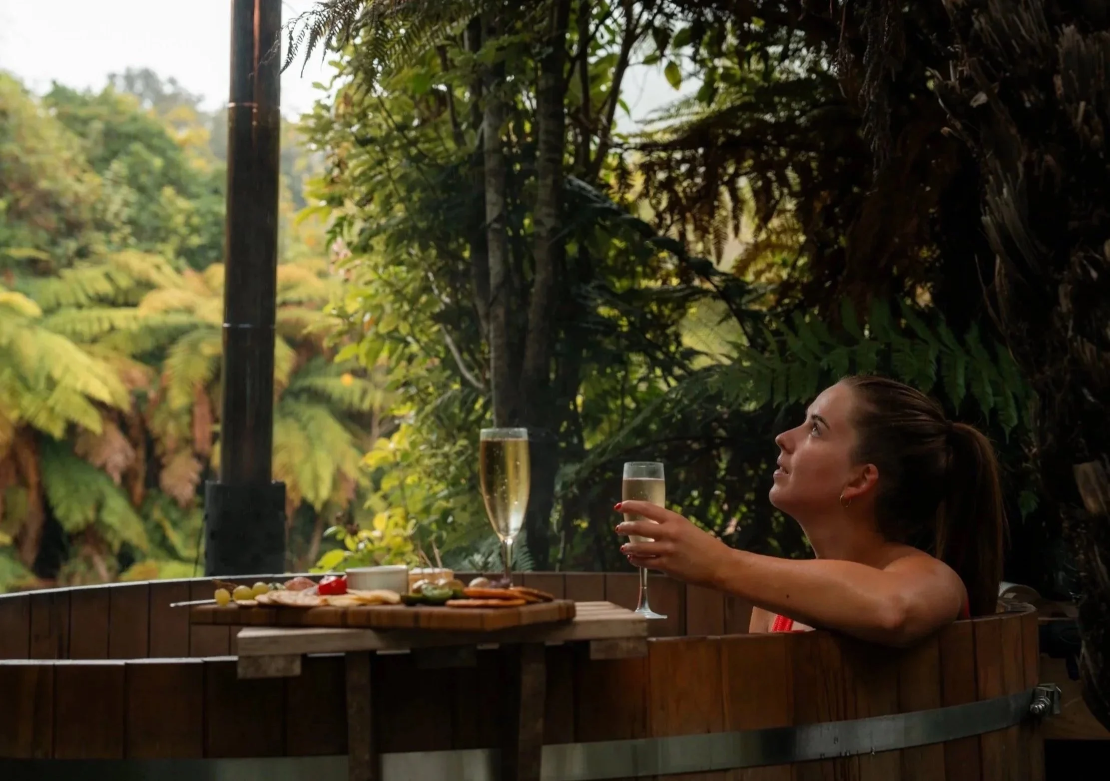 Guest relaxing in a private hot tub at Lake Brunner Eco Lodge, enjoying drinks surrounded by native West Coast bush.