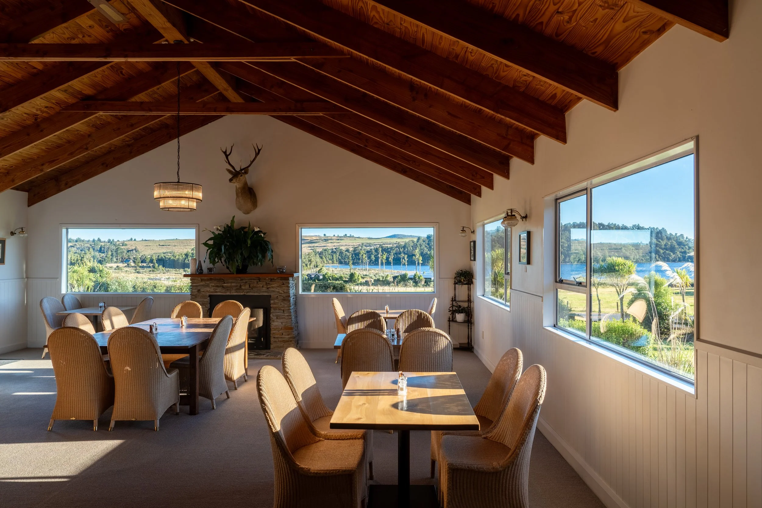 Sunlit dining room inside Lake Brunner Eco Lodge with timber ceilings, and intimate table settings overlooking New Zealand’s West Coast landscape. Warm hosted eco-lodge accommodation designed for peaceful wilderness escapes