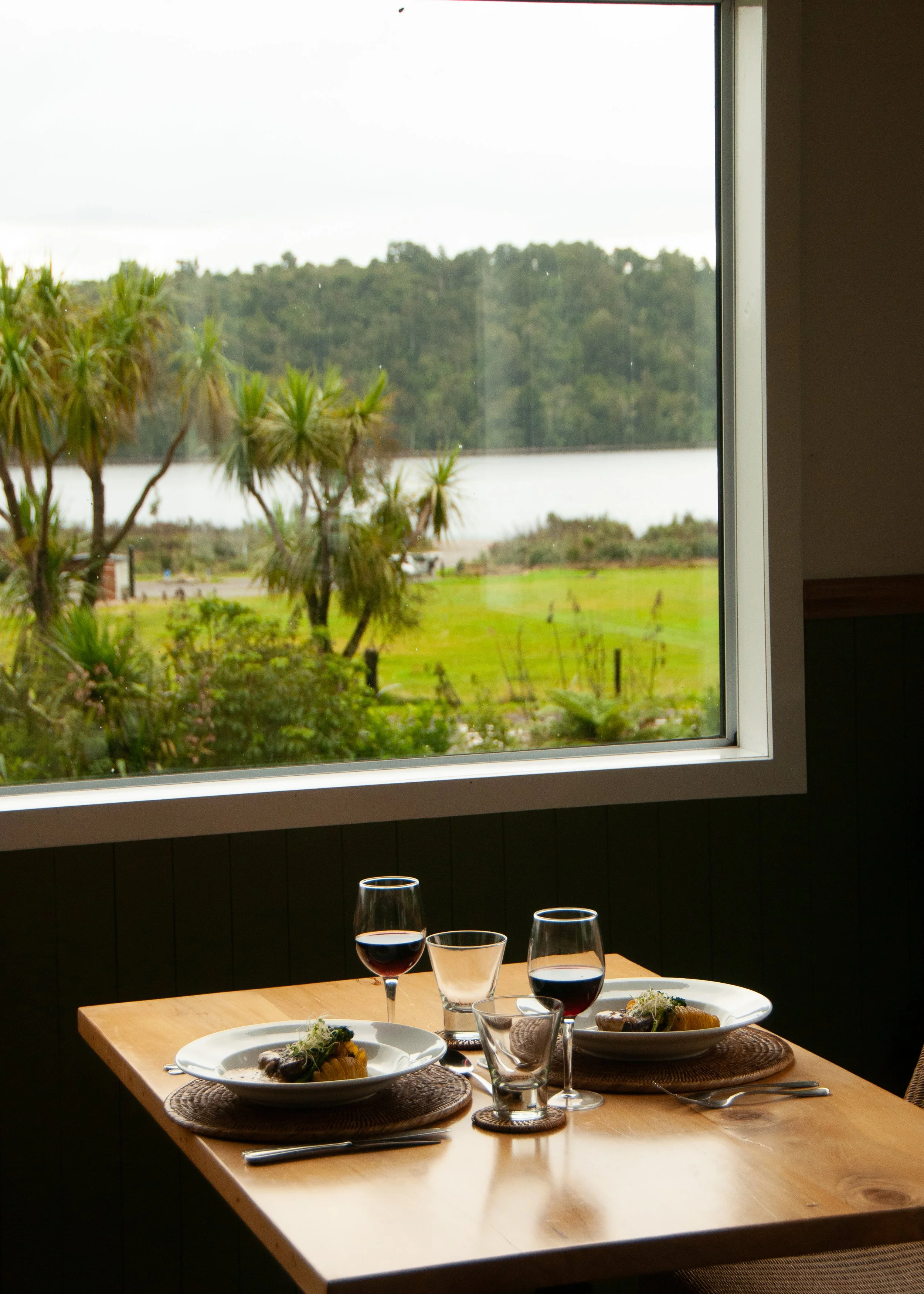 Dinner for two at Lake Brunner Eco Lodge, with beautifully presented dishes and glasses of red wine.