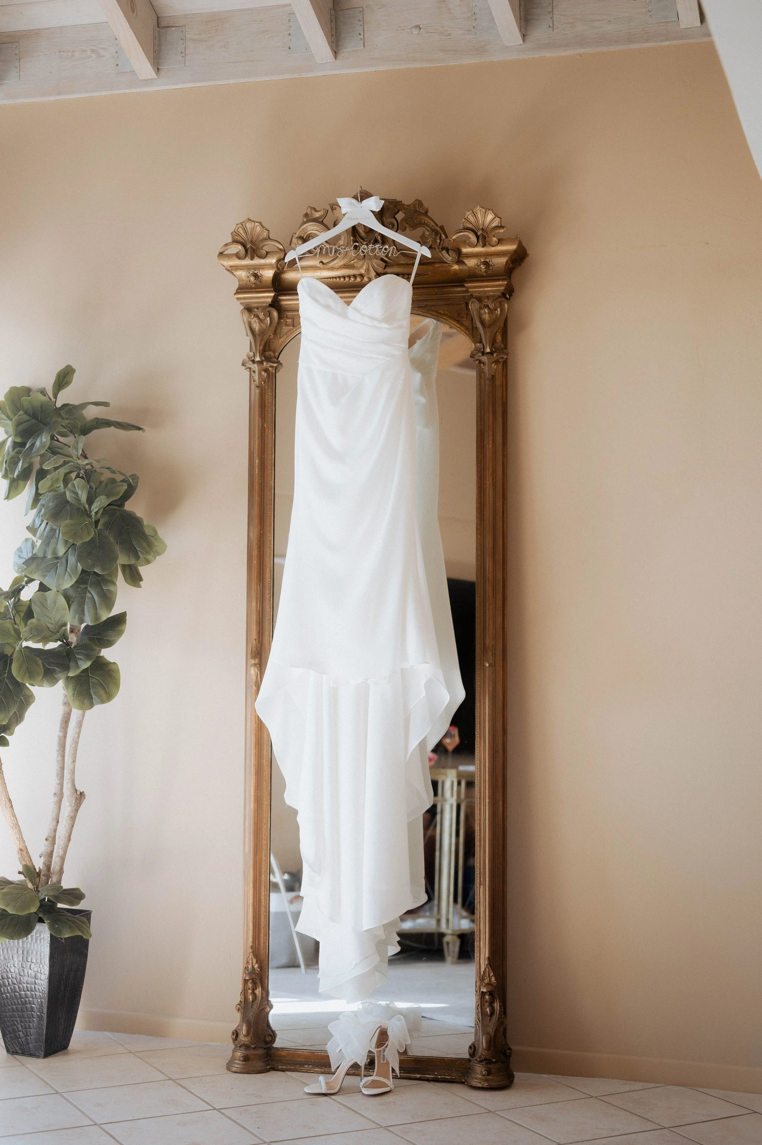 Wedding dress hanging on a mirror with a pair of white high heels below