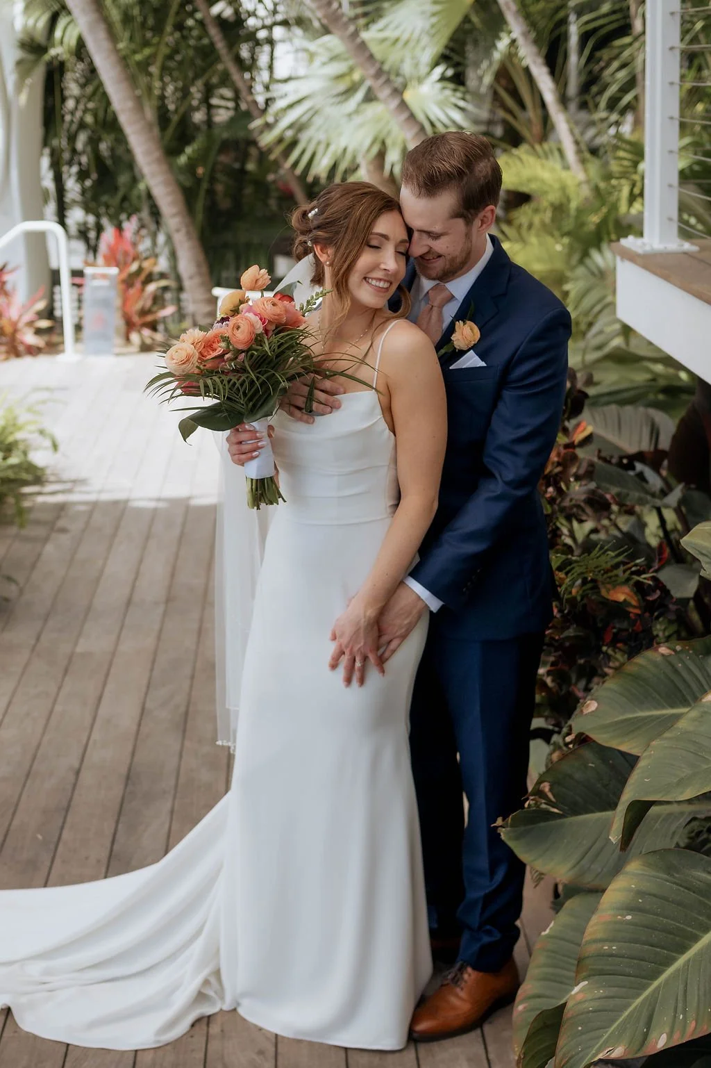 A newlywed couple sharing a joyful moment, the bride holding a bouquet of flowers, surrounded by lush tropical plants. St andrews state park weddings, Panama City beach weddings, PCB Photographers, PCB weddings