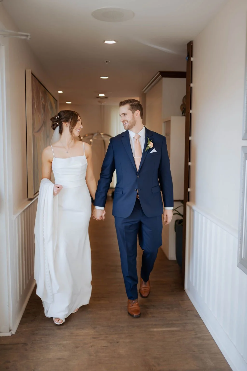 A bride and groom holding hands and walking down a hallway, looking at each other and smiling, celebrating their wedding day.Panama City beach weddings, PCB Photographers, PCB weddings