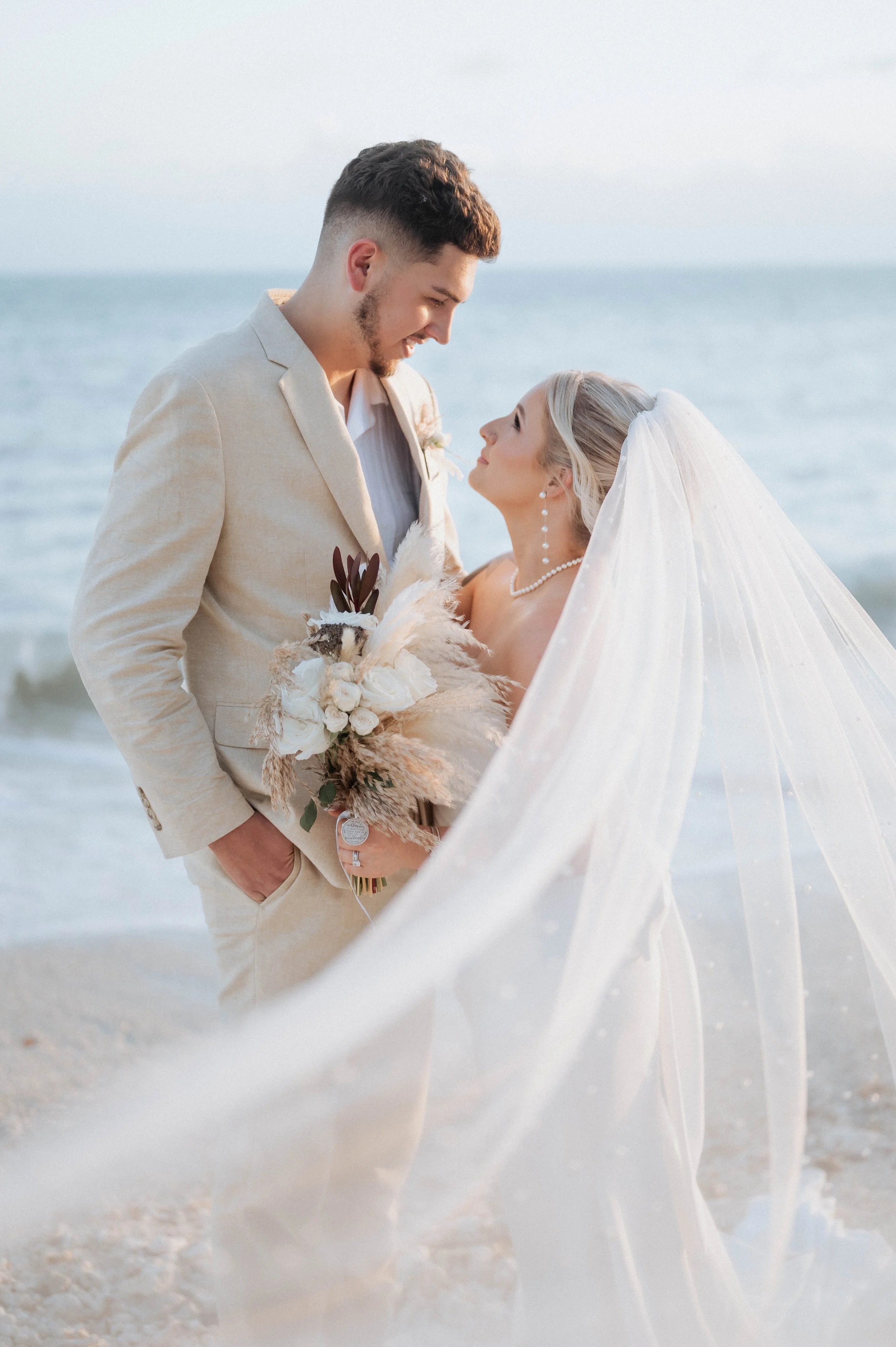 Couple in wedding attire standing on the beach, gazing into each other's eyes, with ocean waves in the background. Panama City beach wedding photographer, pcb weddings all inclusive