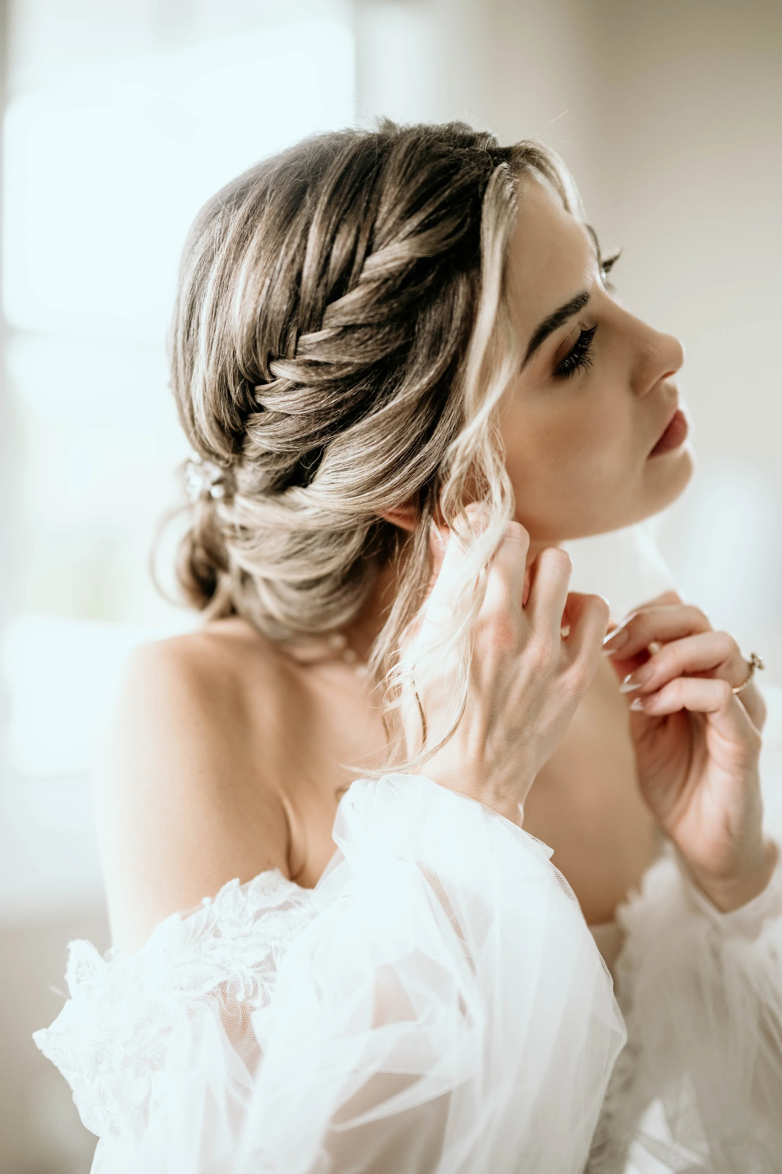 A bride with styled hair, wearing a white dress, adjusting her earring in a softly lit room.Panama City beach weddings, PCB Photographers, PCB weddings