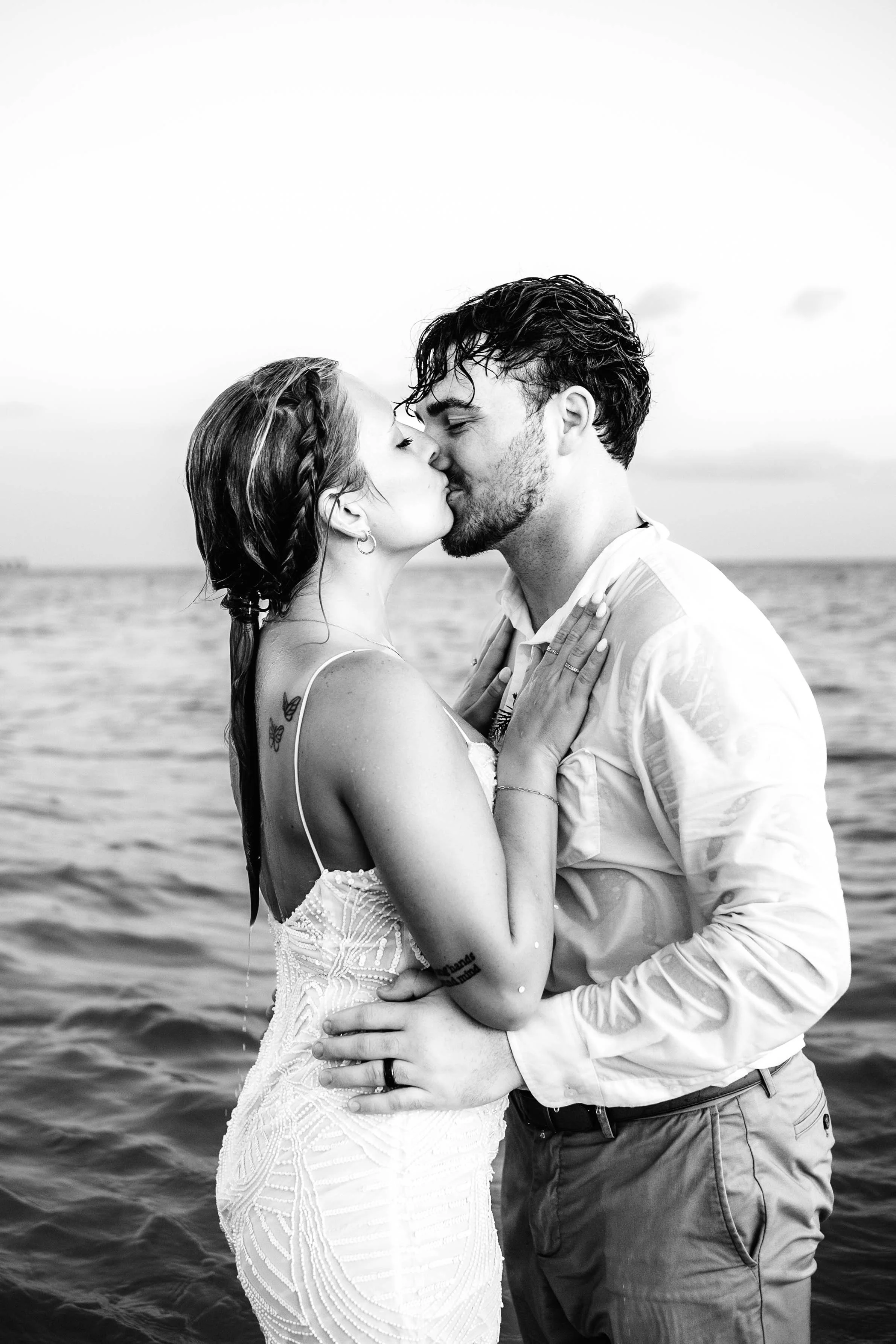 A black and white photo of a couple kissing by the water, with the woman wearing a wedding dress and the man in a white shirt and khakis. St andrews state park weddings, Panama City beach weddings, PCB Photographers, PCB weddings