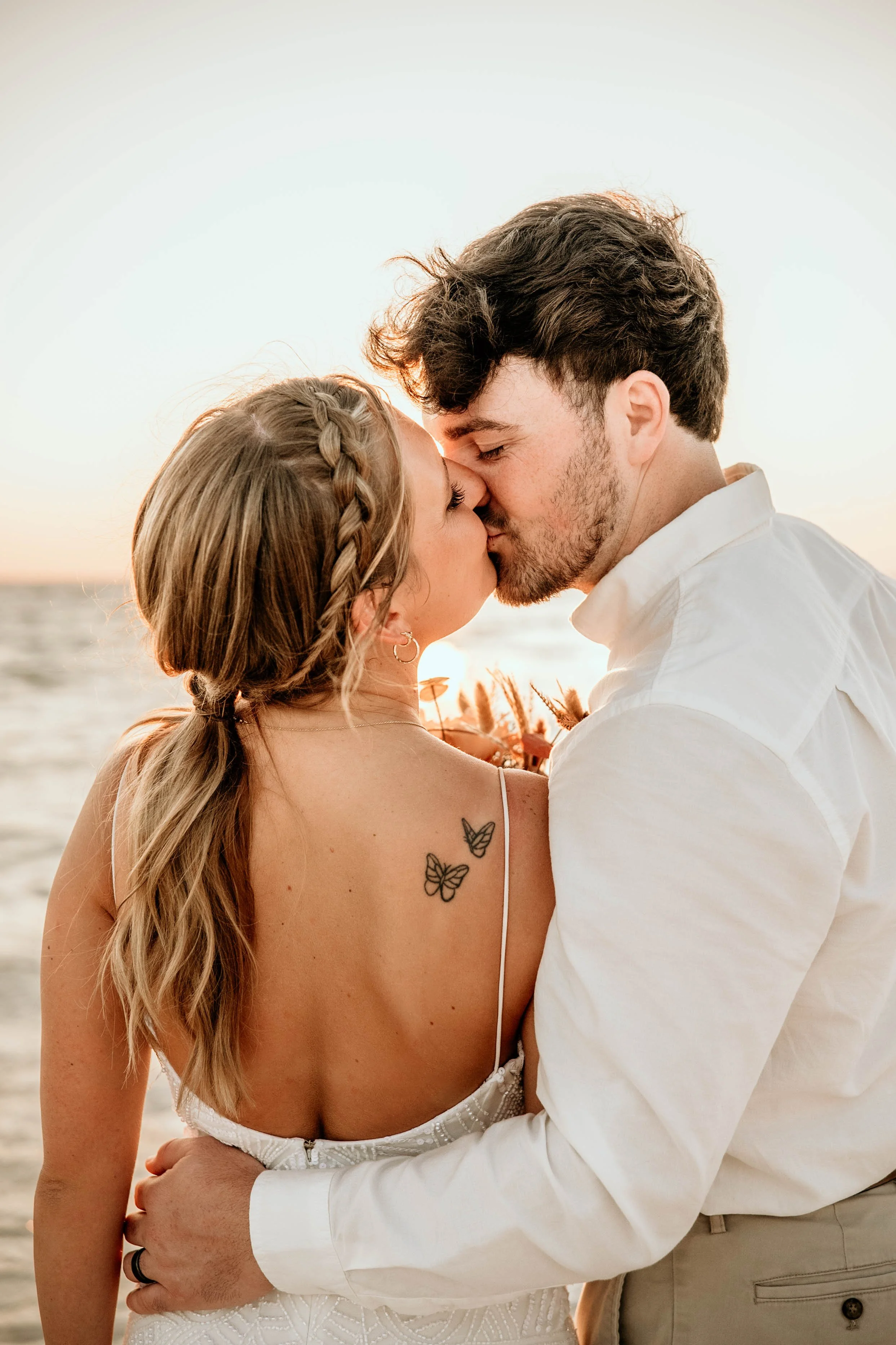 A couple kissing on the beach at sunset, embracing each other close. Panama city beach wedding beach photography