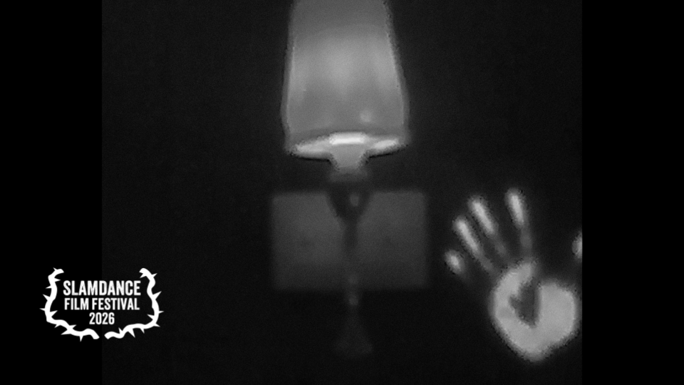 Black and white photo of a lampshade above a table, with a handprint on a surface to the right, and a logo in the lower-left corner reading 'SLAMDANCE FILM FESTIVAL 2026'.