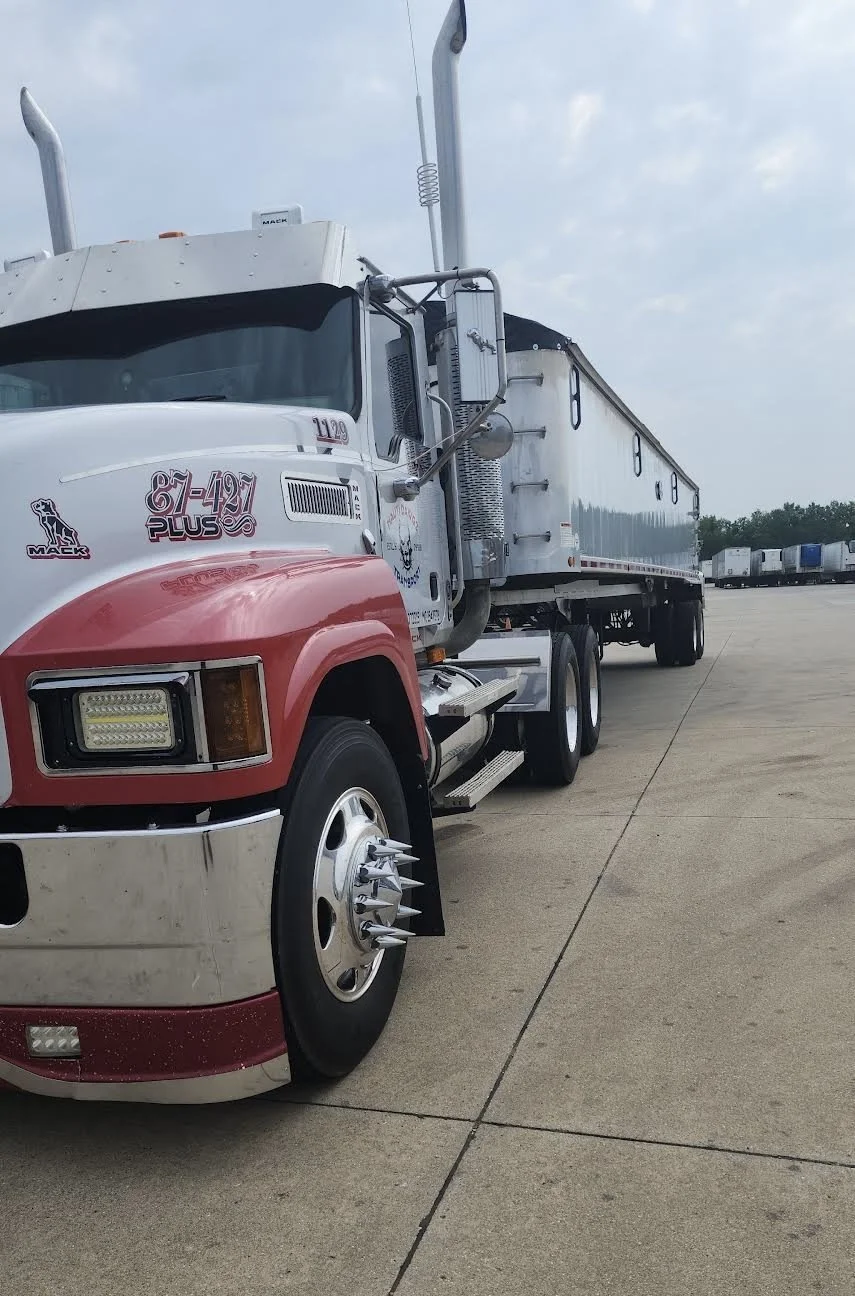 A semi-truck with a white and red cab parked on a concrete lot, with multiple trailers in the background under a cloudy sky.