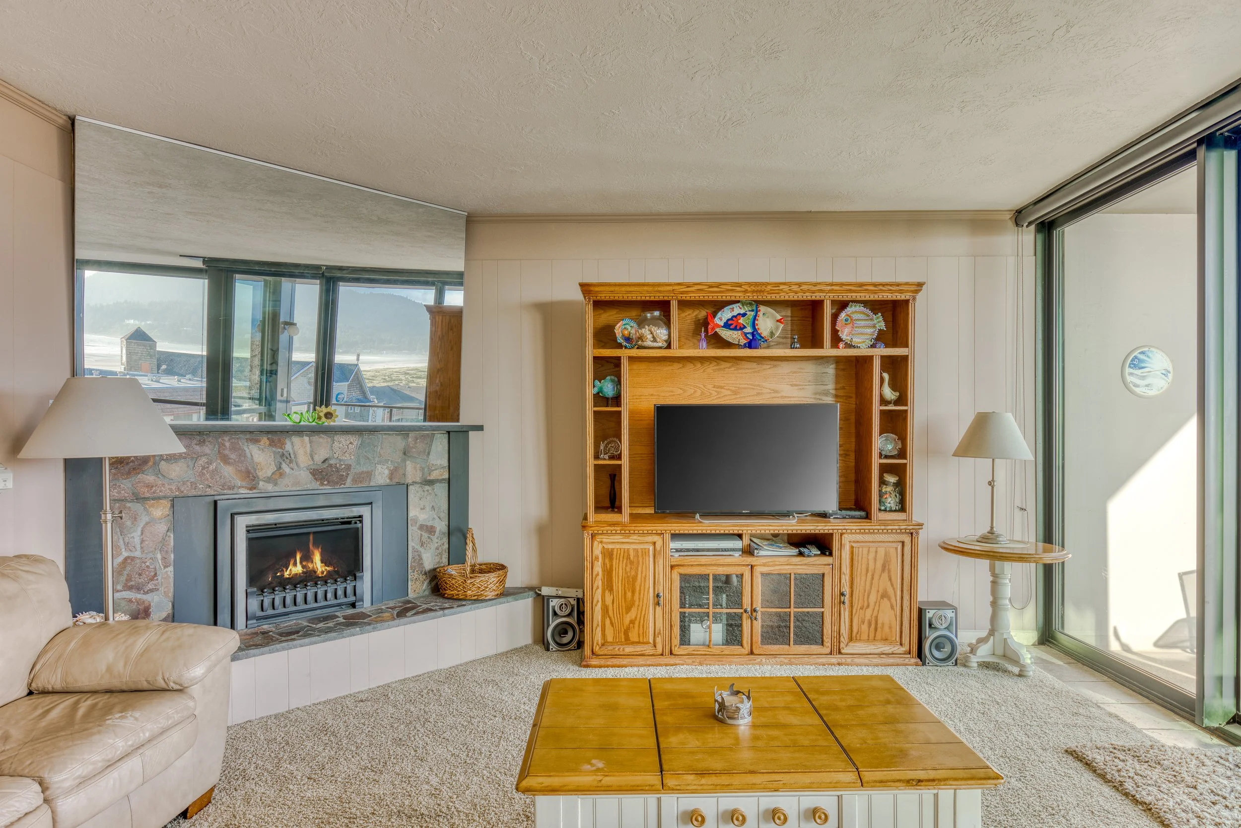Cozy living room with stone fireplace, TV stand with shelves, large TV, and glass sliding doors.