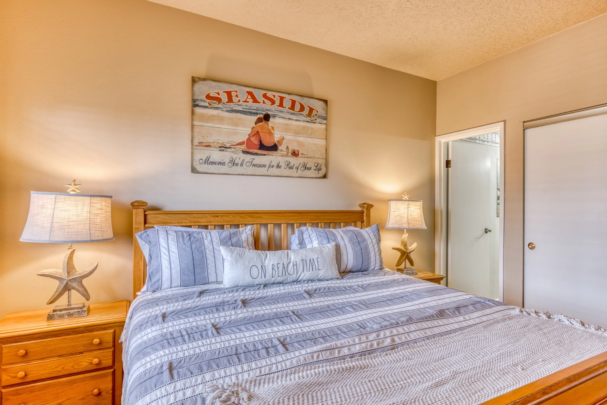 Beach-themed bedroom with a wooden bed, striped bedding, and a "Seaside" wall art. Starfish-shaped lamps on nightstands add a coastal touch.