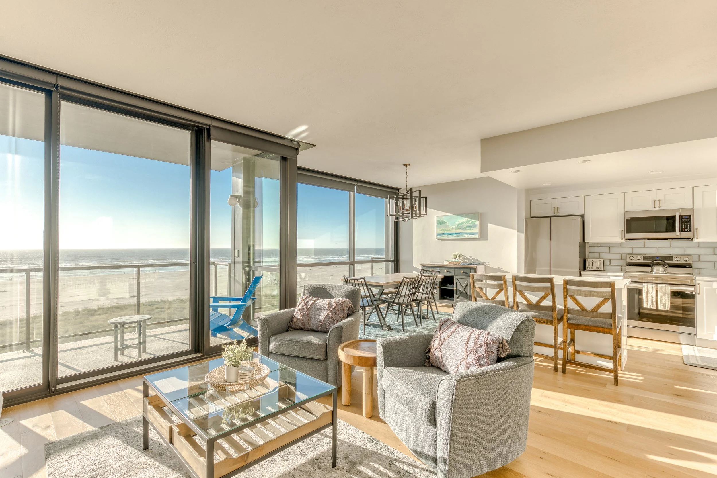 Modern beachside living room and kitchen with ocean view, featuring glass doors, stylish furniture, and bright decor.
