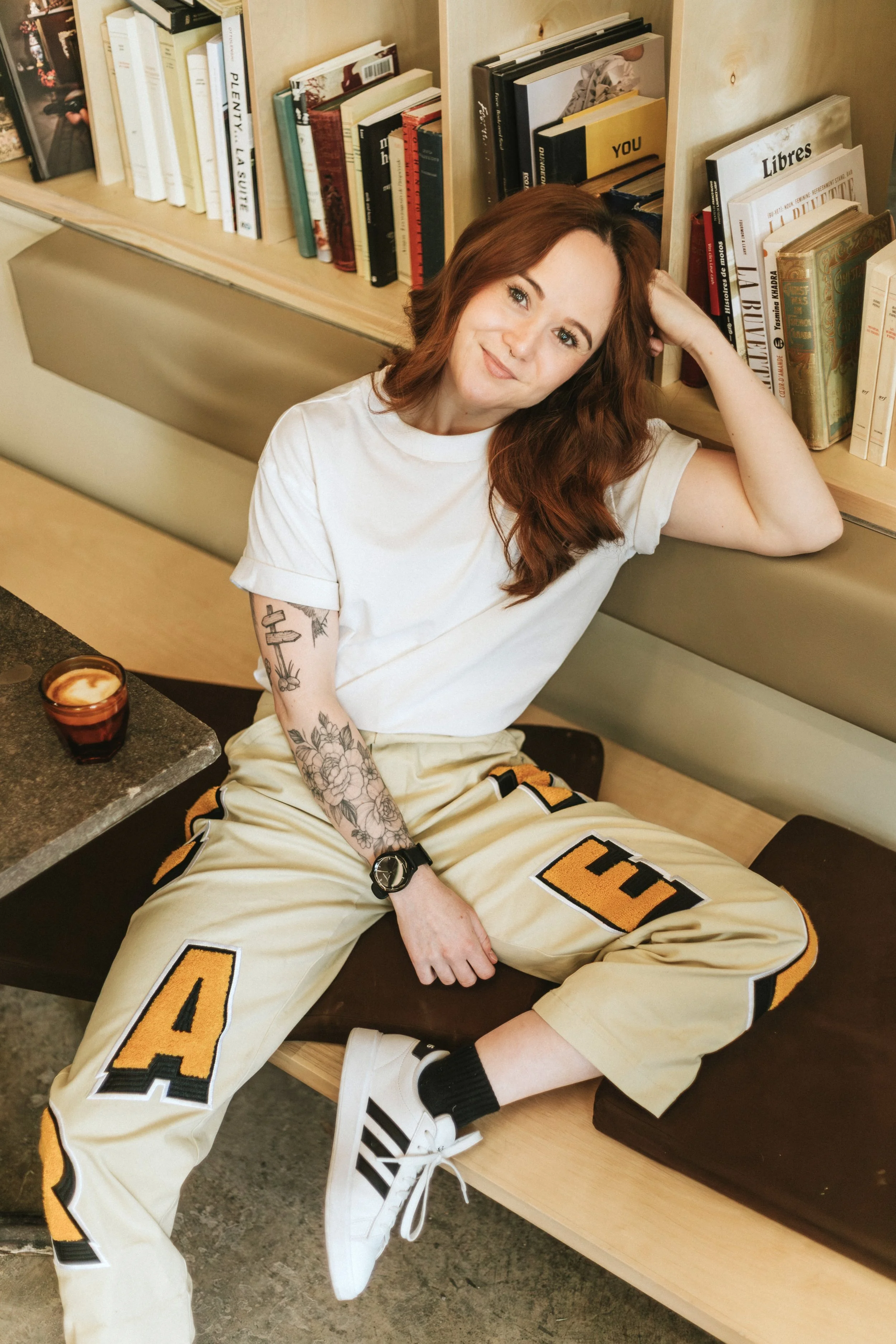 Mim Kempson sits in a cafe at bookshelf with a cup of coffee