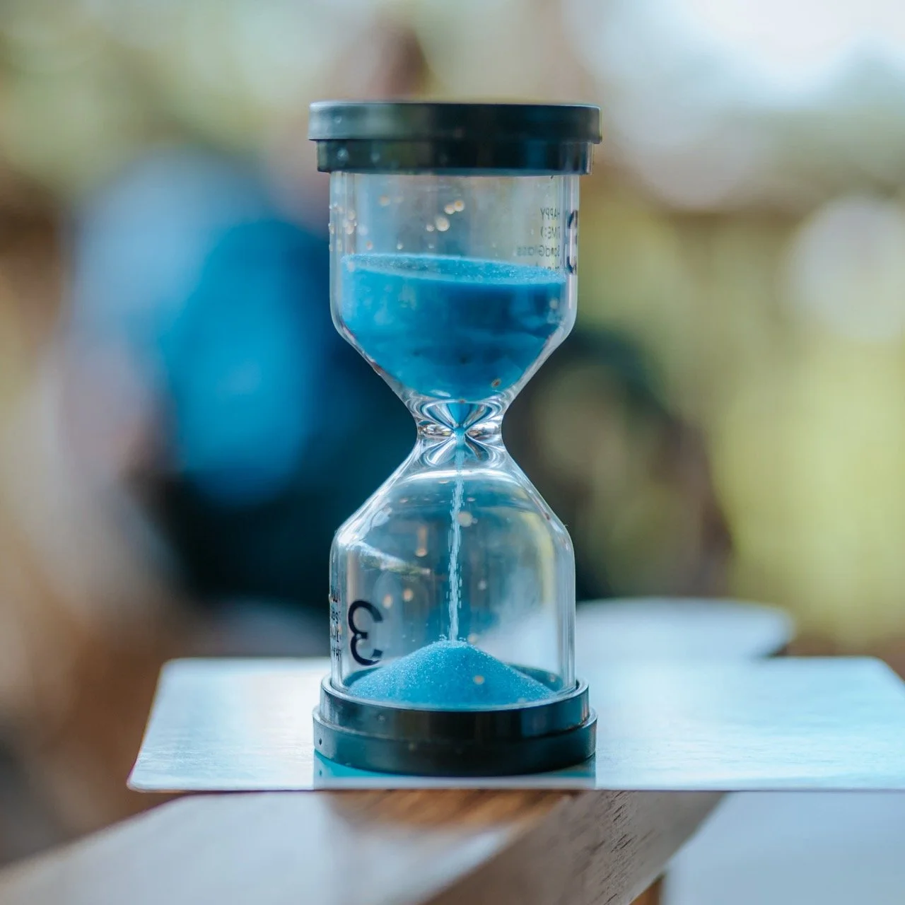 Close-up of an hourglass with blue sand flowing from the top to the bottom chamber, placed on a white surface.