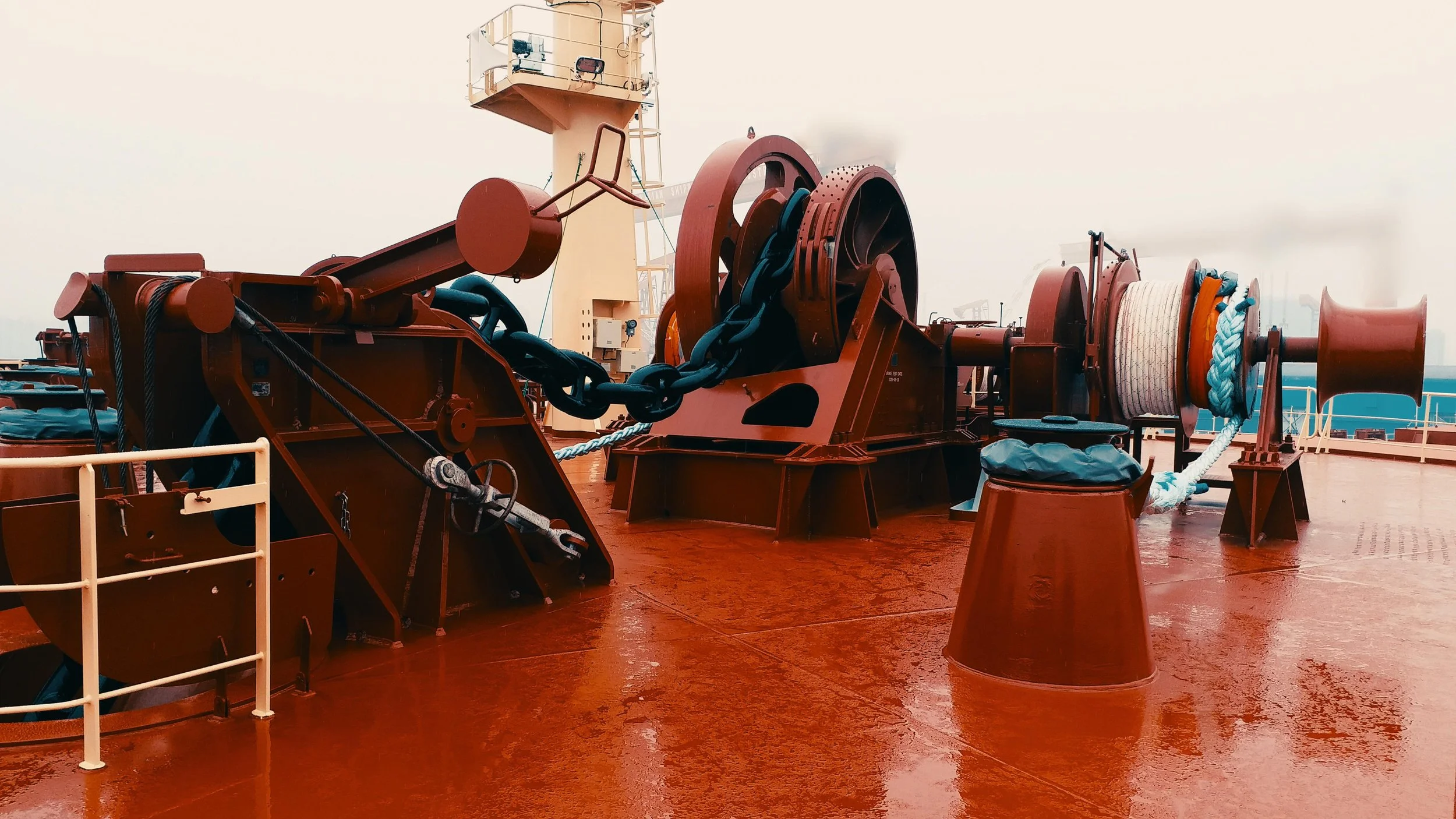 Close-up of heavy-duty ship anchor chain and windlass on a red deck.