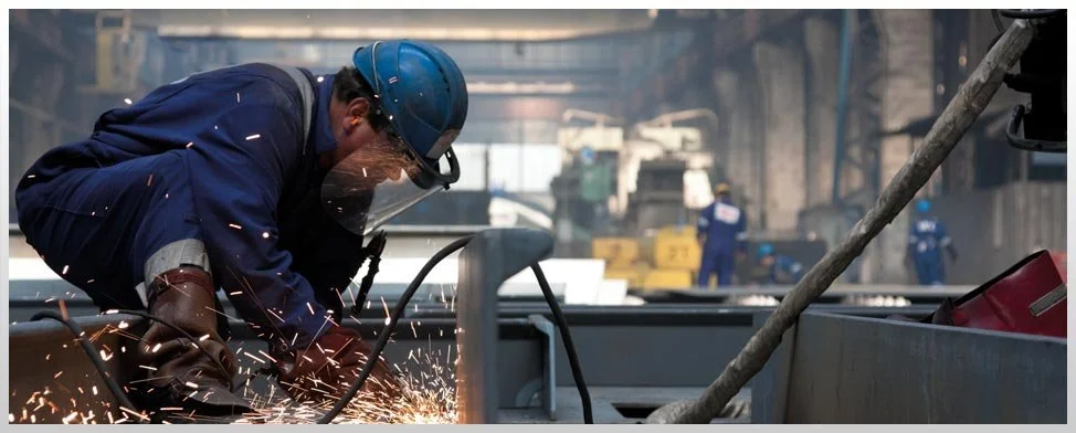 A worker welding metal in an industrial setting with sparks flying.