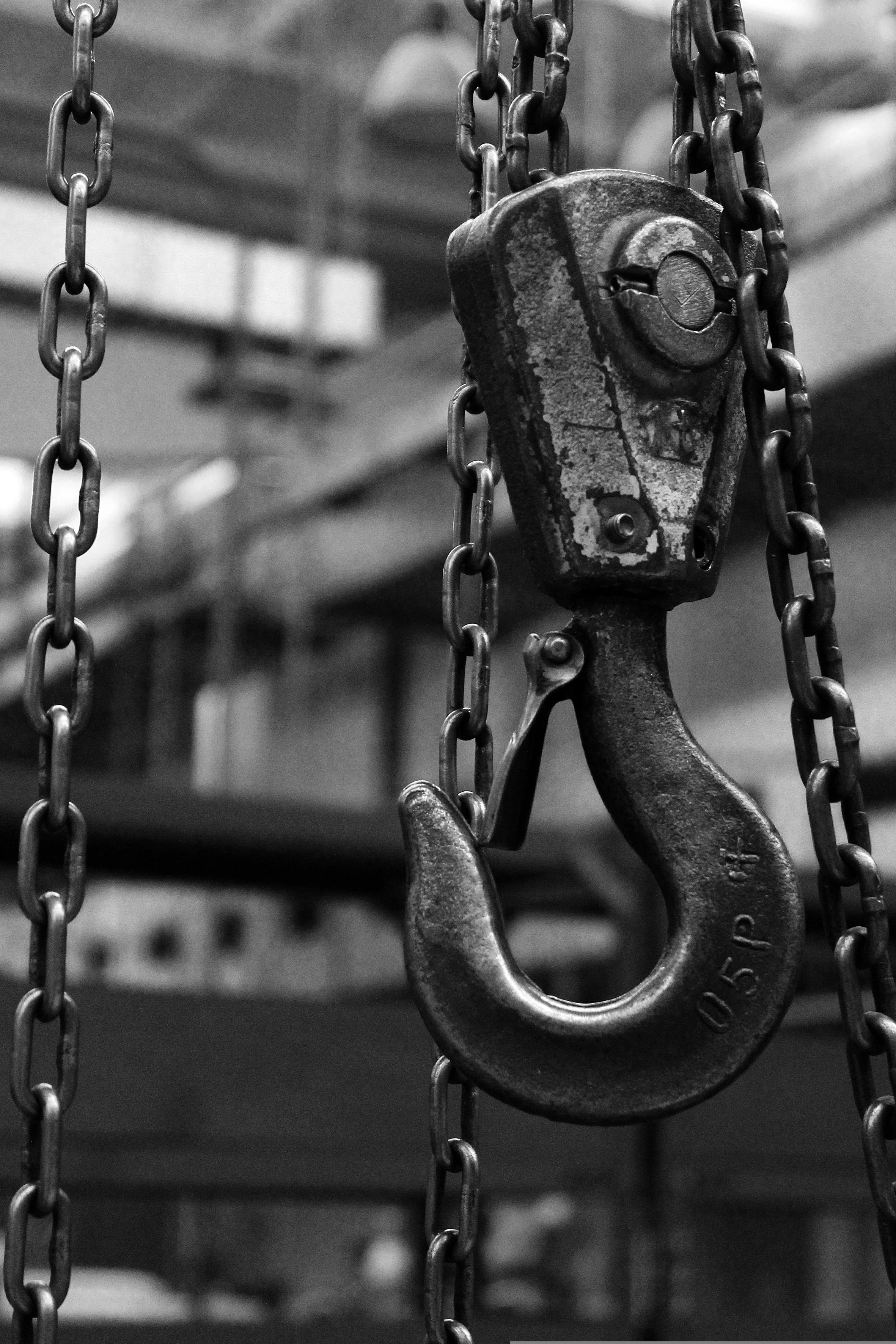 A rusty industrial hook hanging from metal chains in a black and white photograph.
