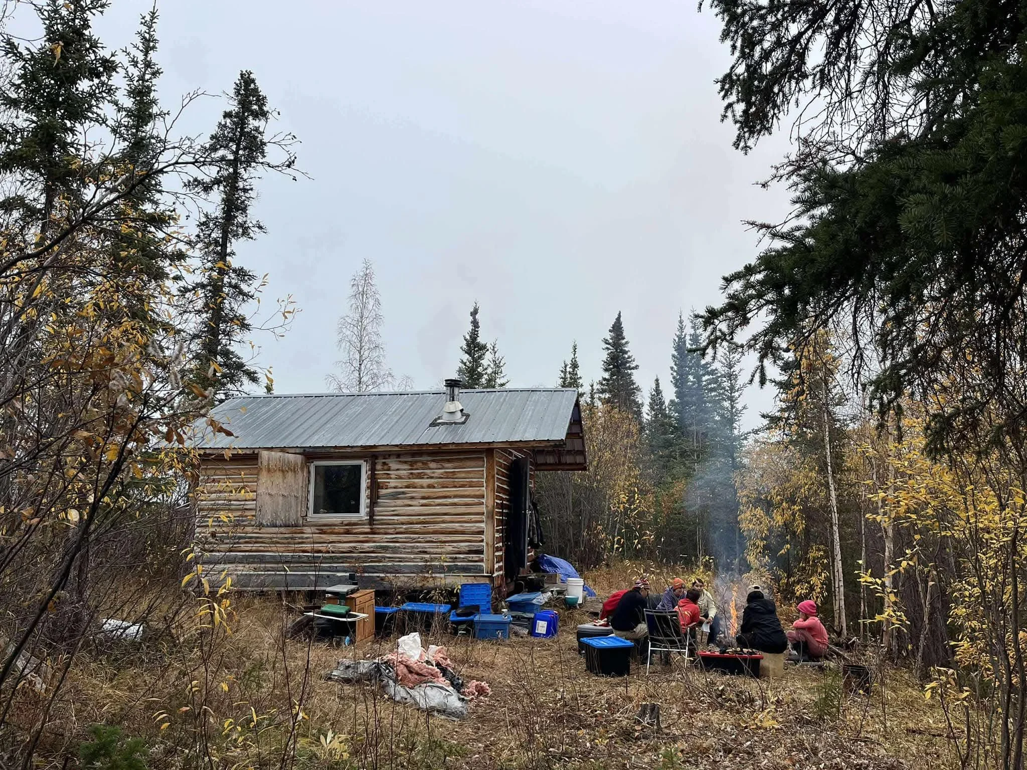  learners around a fire outside in front of a cabin in the woods