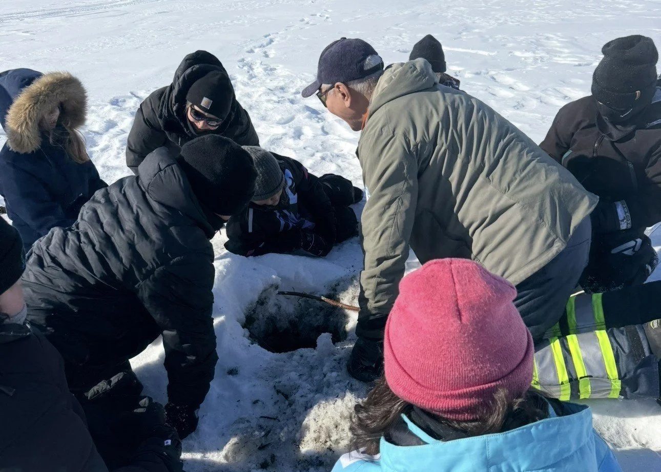 Learners gathered around a beaver hole in the ice with an elder