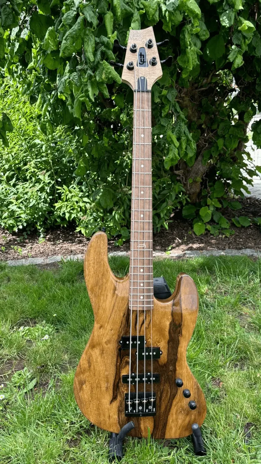 Ein E-Bass in Black-Limba-Holz vor einem grünen Busch