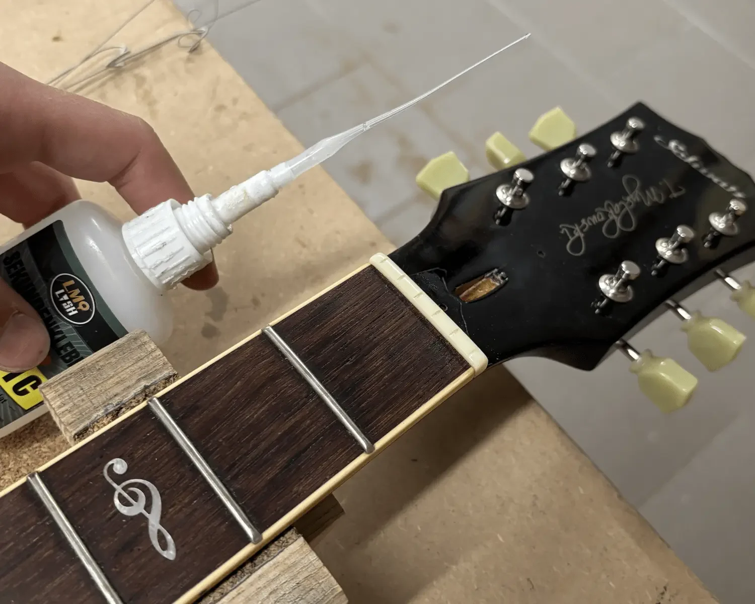 E-Gitarre mit Sattel drinnen. Daneben hält jemand eine Klebetube