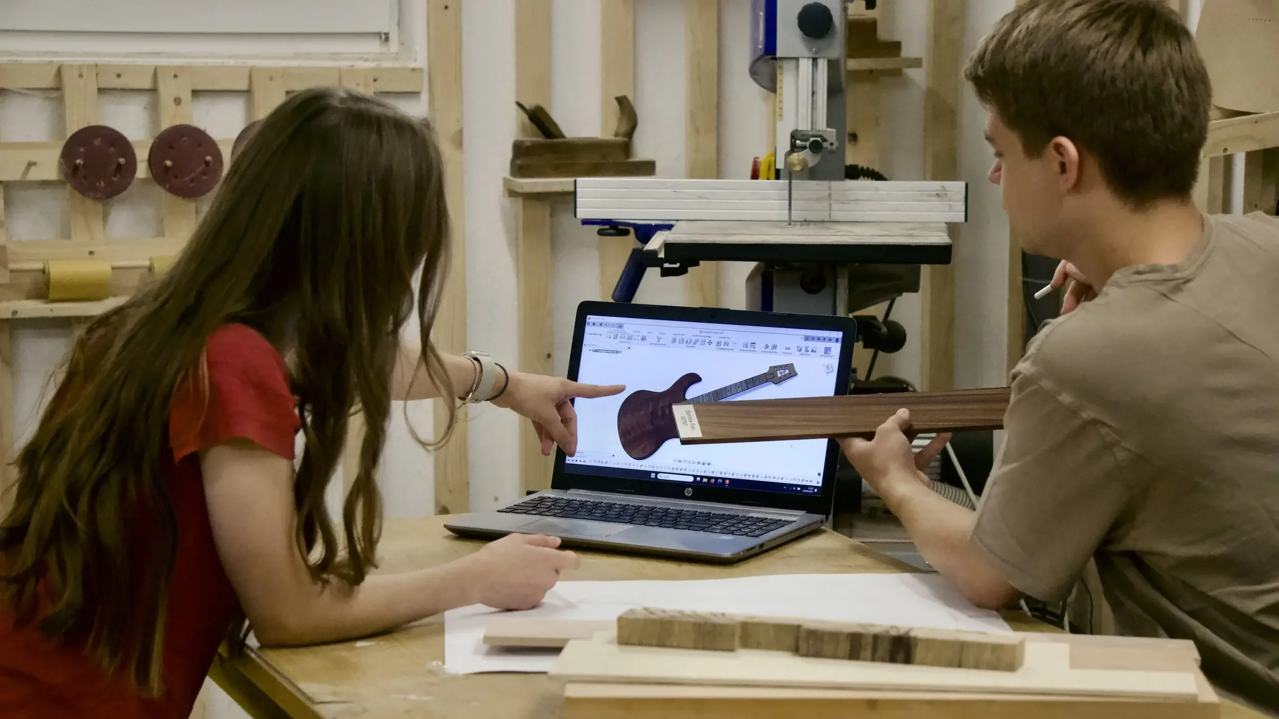 Zwei Personen vor Laptop, besprechen Design der E-Gitarre