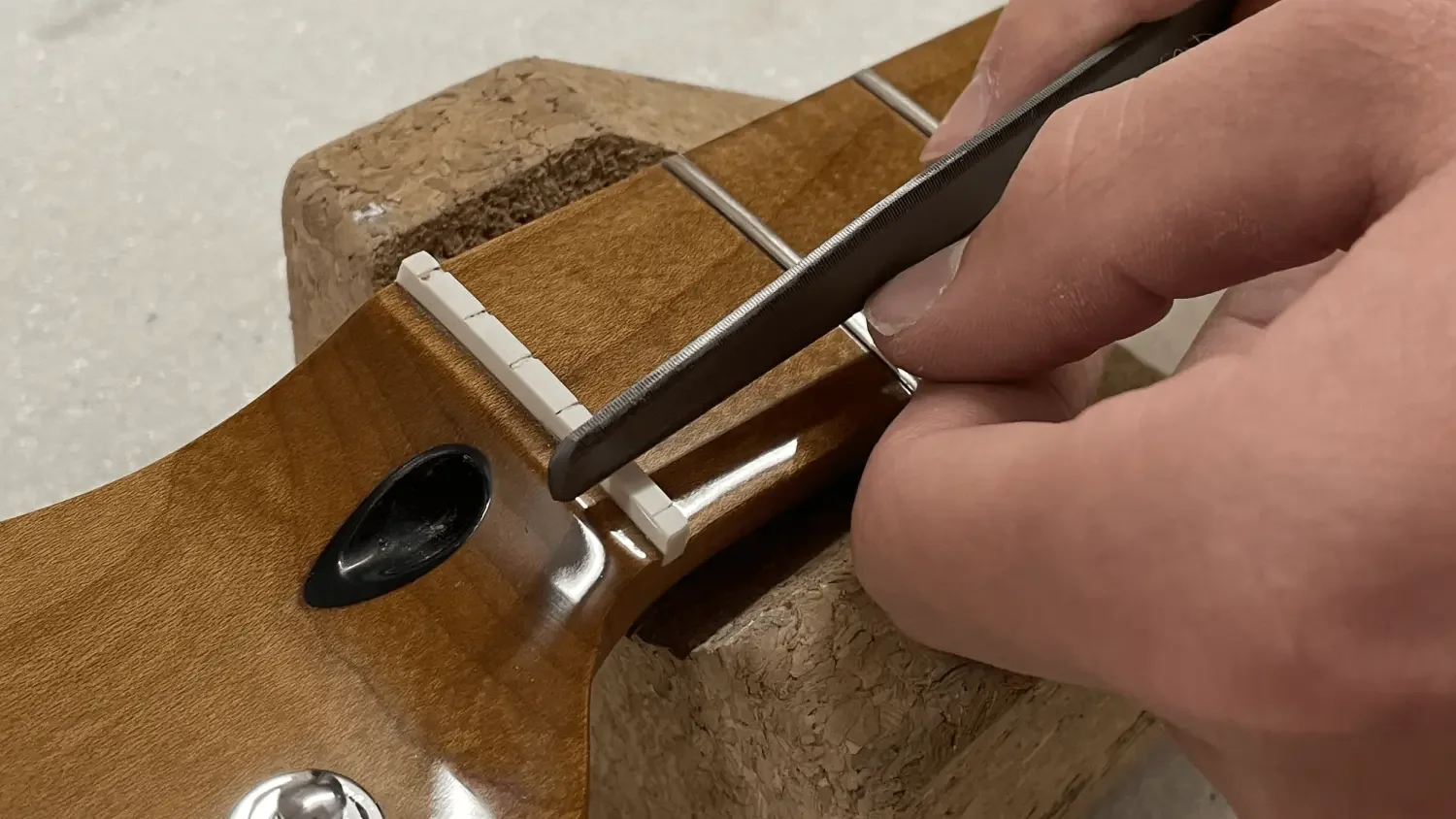 Der Sattel einer E-Gitarre wird mit einer Feile bearbeitet