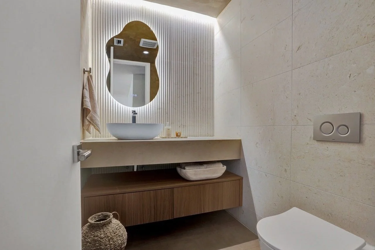Bespoke backlit wavy mirror on a fluted travertine feature wall in Essendon renovation