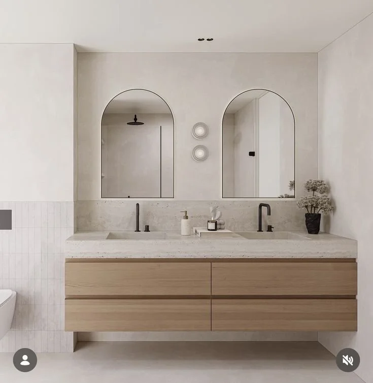 Modern bathroom with double vanity, large mirror, and minimal decor. Two black faucets, soap dispensers, and a potted plant are on the counter.