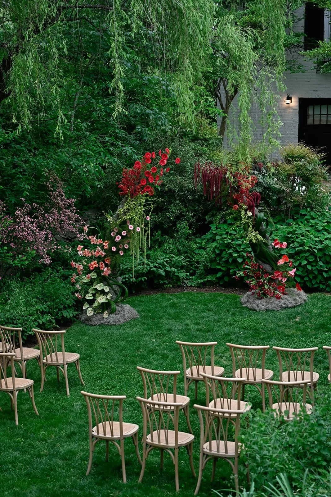 An outdoor garden with lush greenery and colorful flowers, arranged with wooden chairs on a well-kept grass lawn, ready for an event or gathering at The Clifton Inn in Charlottesville Virginia