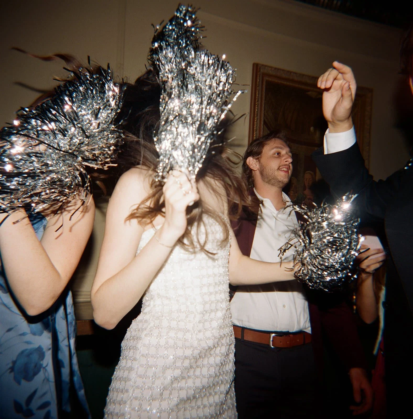 People dancing at a celebration, holding silver tinsel pom-poms.