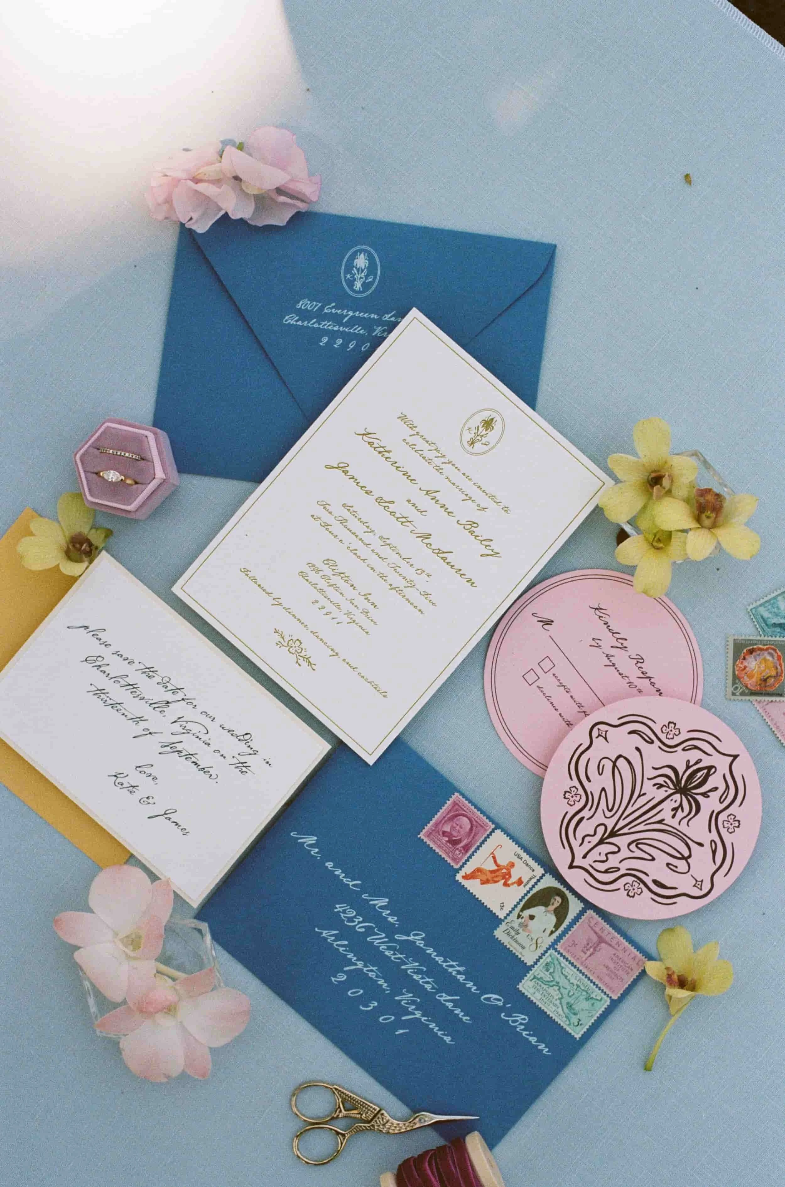 Invitation cards, envelopes, stamps, flowers, and sewing scissors on a table, preparing for a wedding celebration.