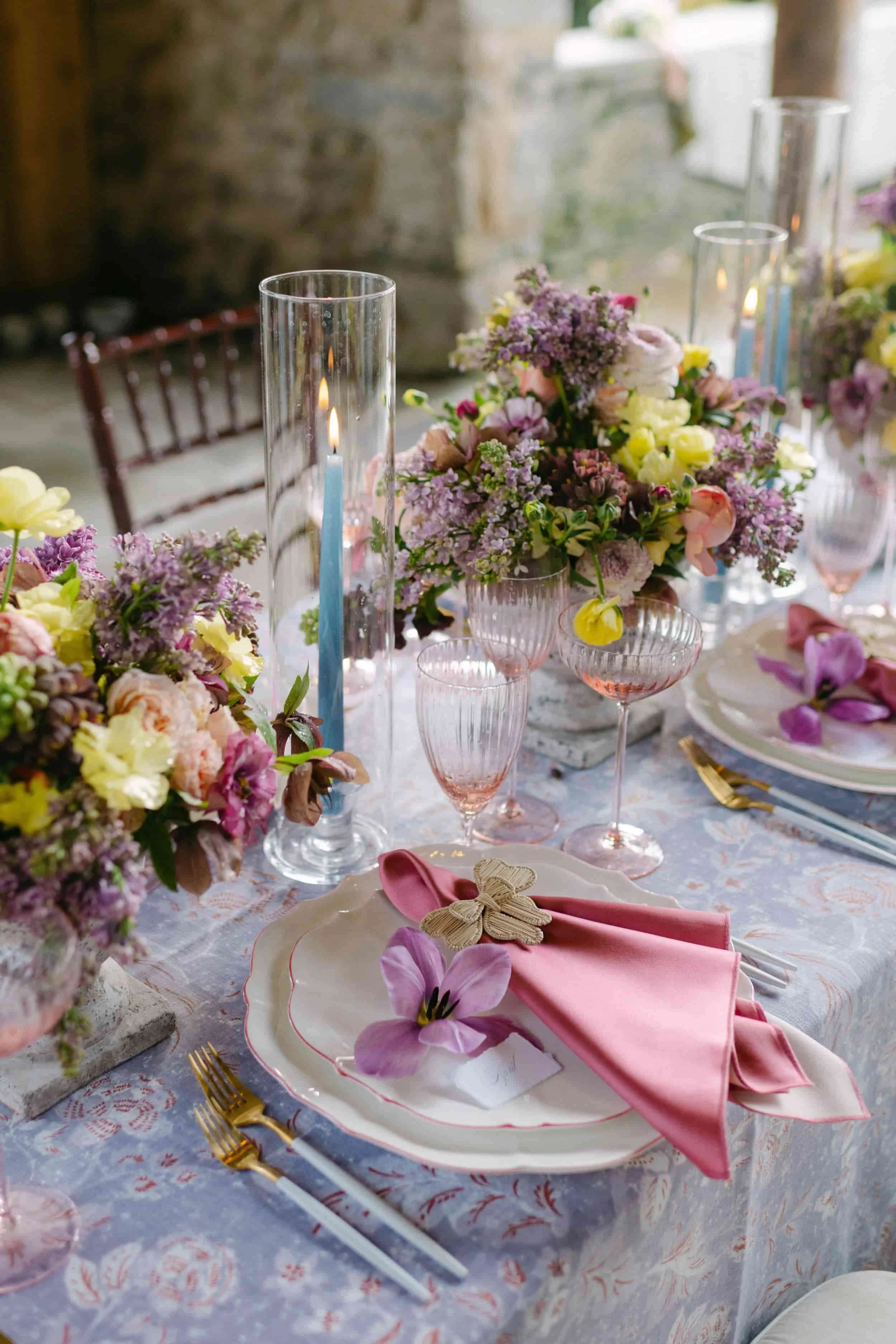 Elegant table setting with pink and purple floral arrangements, pink napkins, clear glassware, and gold utensils, set for a formal event or wedding at The Goodstone Inn, Middleburg VA