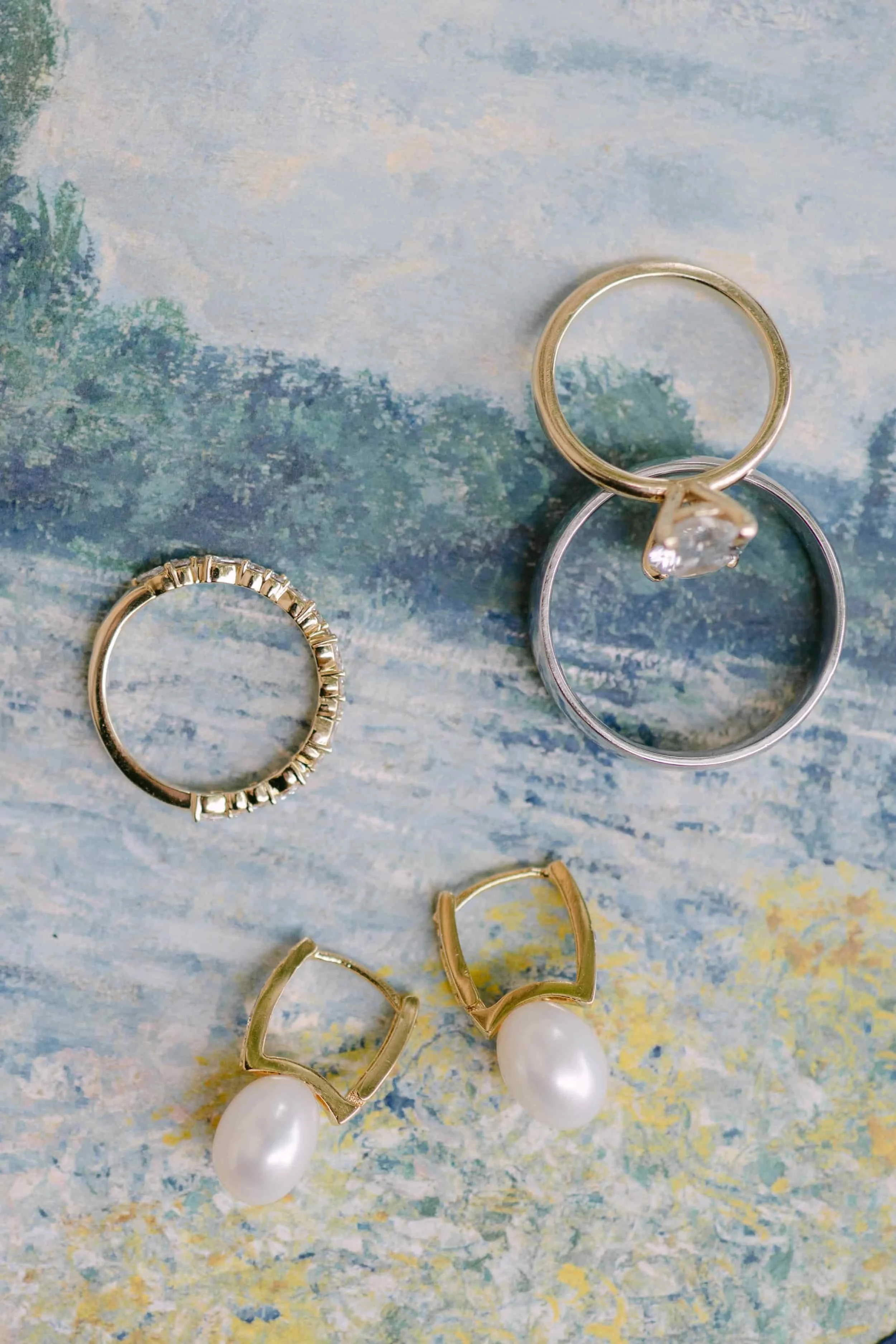 Close-up of four rings and a pair of pearl earrings on a colorful, textured background.