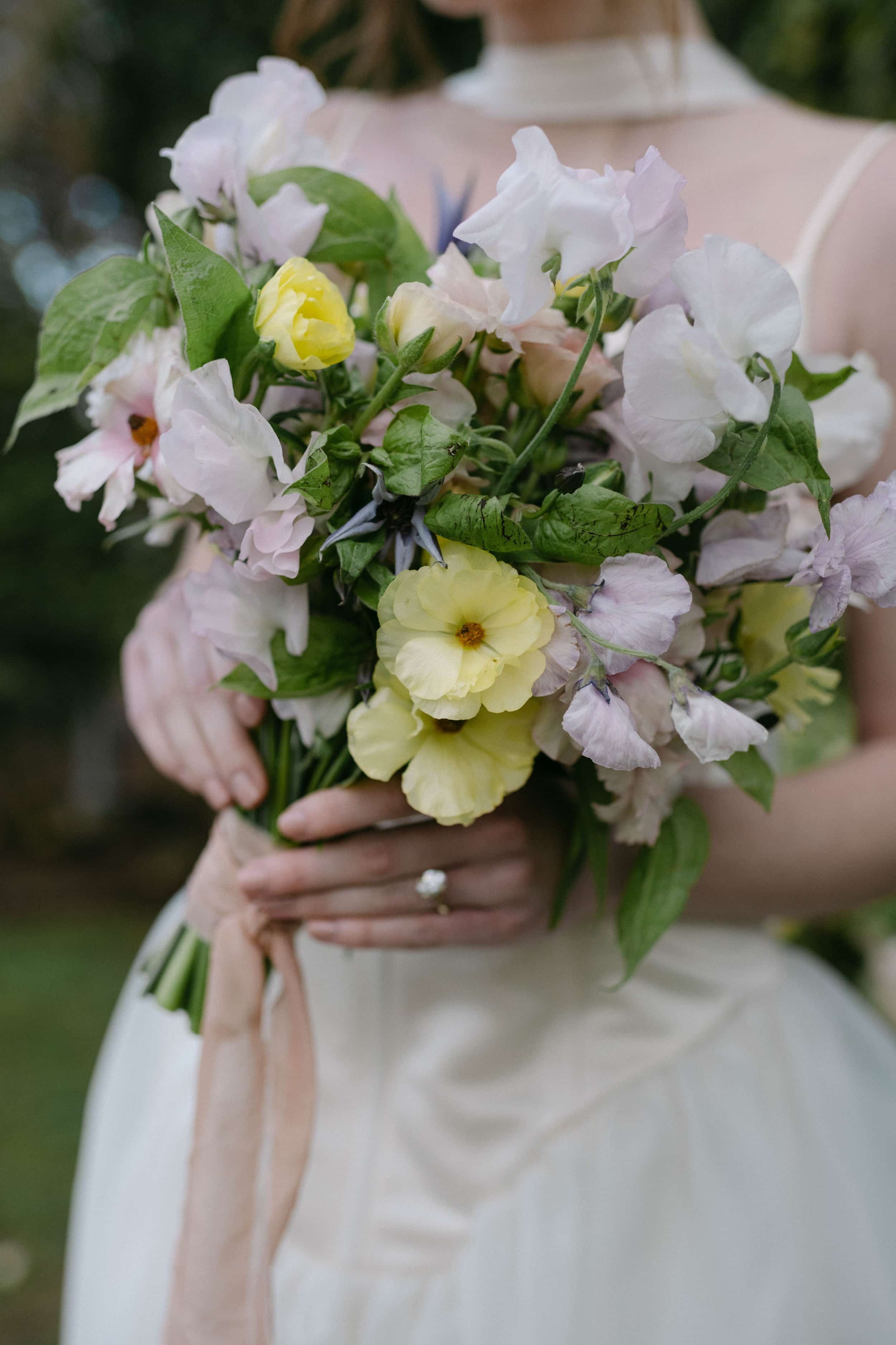 A bride holding a bouquet of pastel-colored flowers including yellow and white blooms, with a ring visible on her finger at Goodstone Inn, Middleburg VA