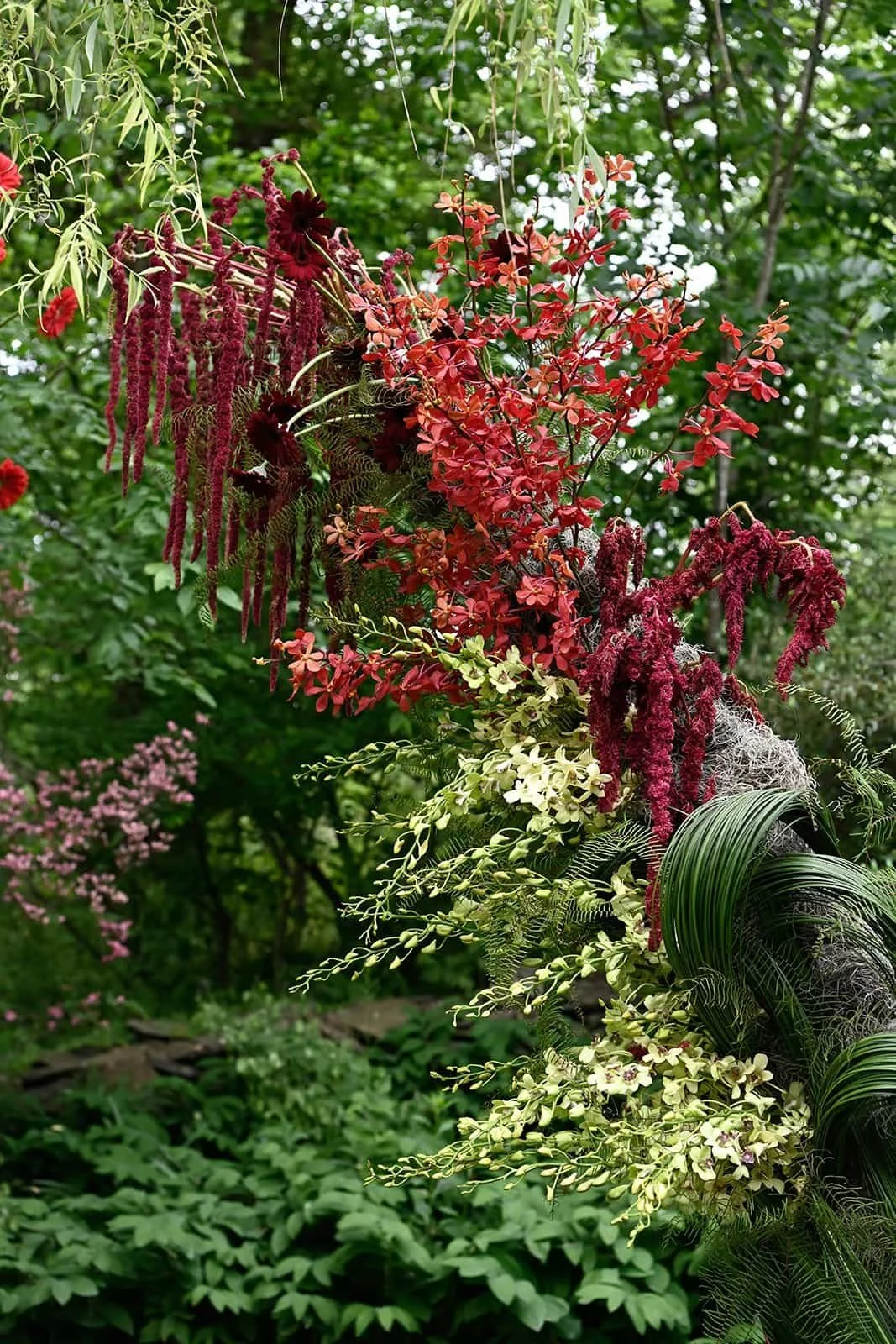 A large floral arrangement with various flowers and greenery, including red, pink, white, and purple flowers, set in a lush green garden background at The Clifton Inn in Charlottesville Virginia