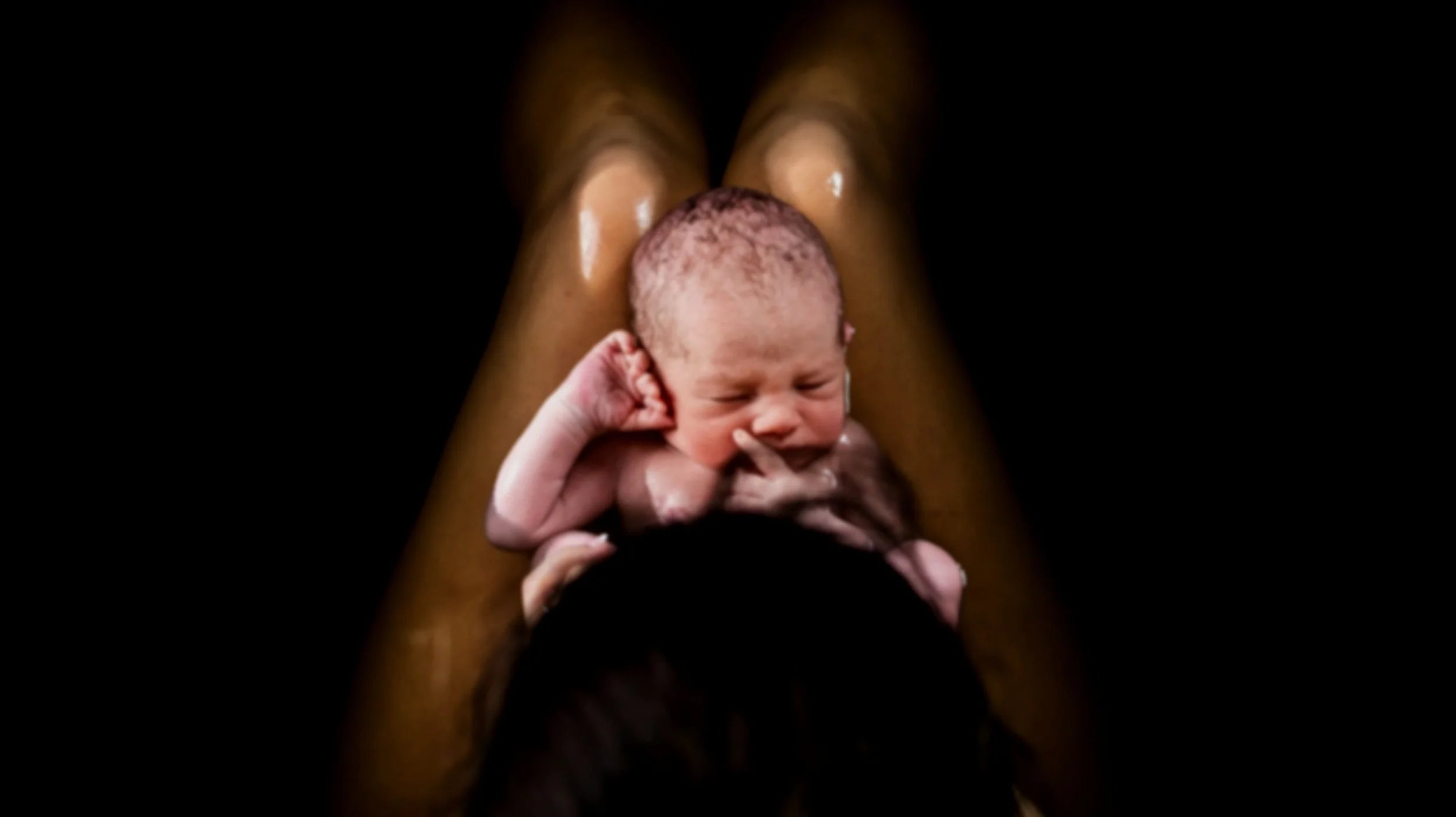 A newborn baby held in someone's hands with a black background.