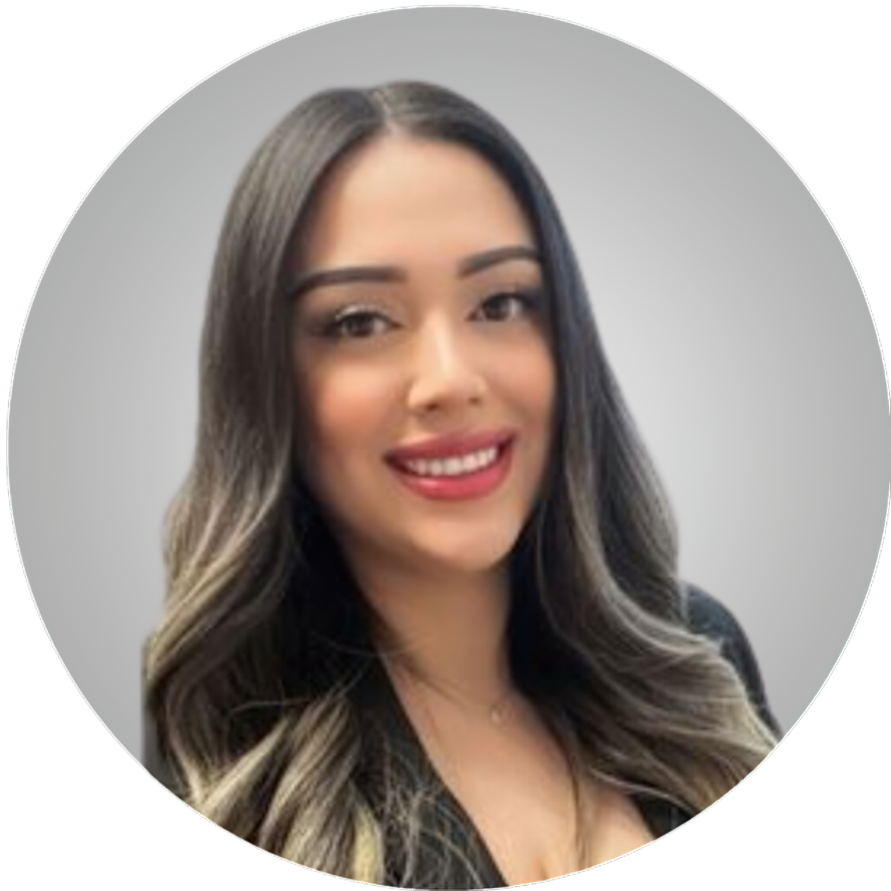 Portrait of a woman with long wavy hair, wearing makeup, smiling, and dressed in a black blazer against a plain gray background.