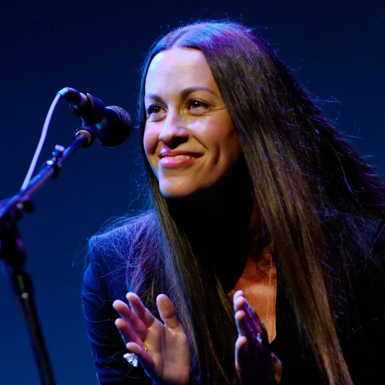 Image of Alanis Morissette smiling on stage in front of a microphone.