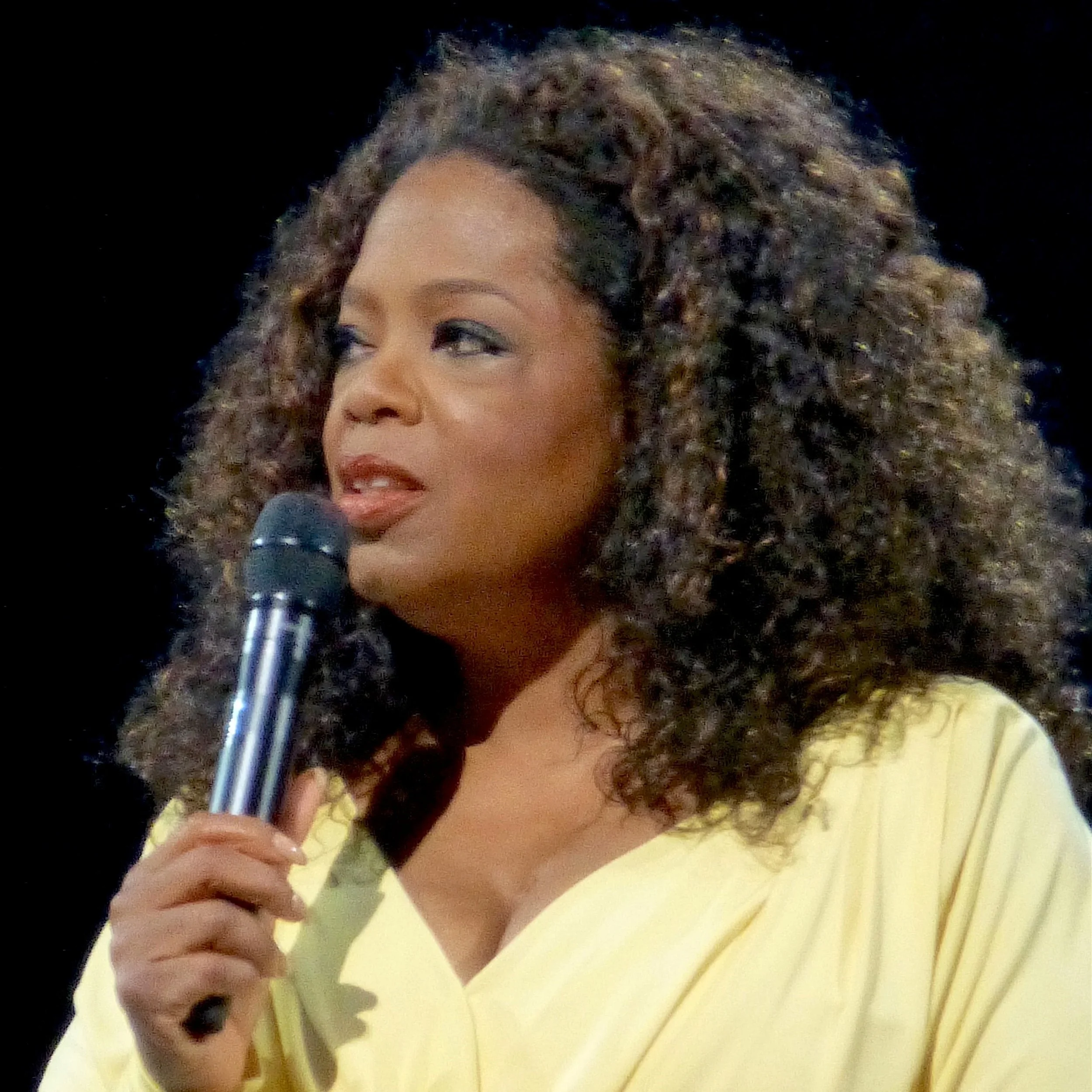 Picture of Oprah Winfrey wearing a yellow shirt and holding a microphone.