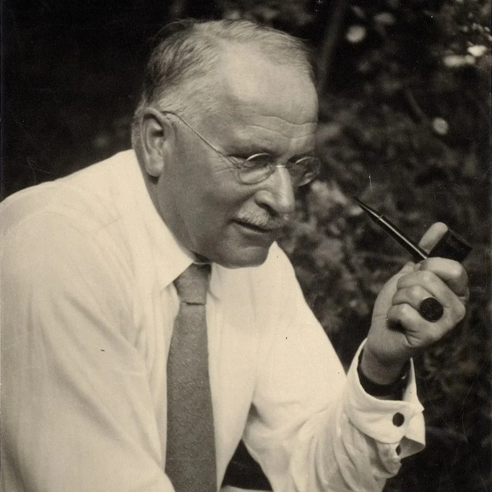 Black and white image of Carl Jung sitting down and holding a pipe.