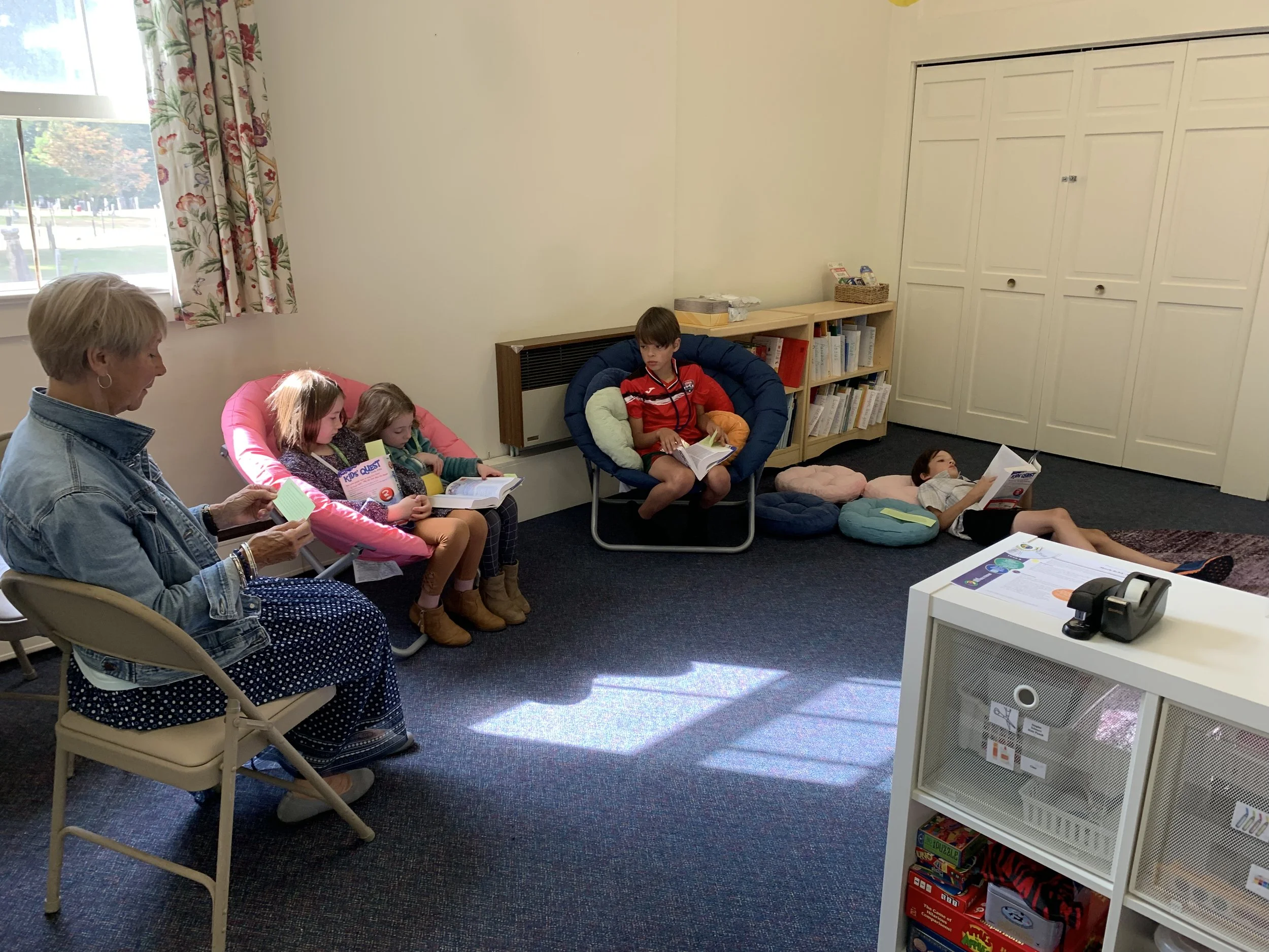 Children and an adult reading in a cozy classroom corner with bean bag chairs and bookshelves.
