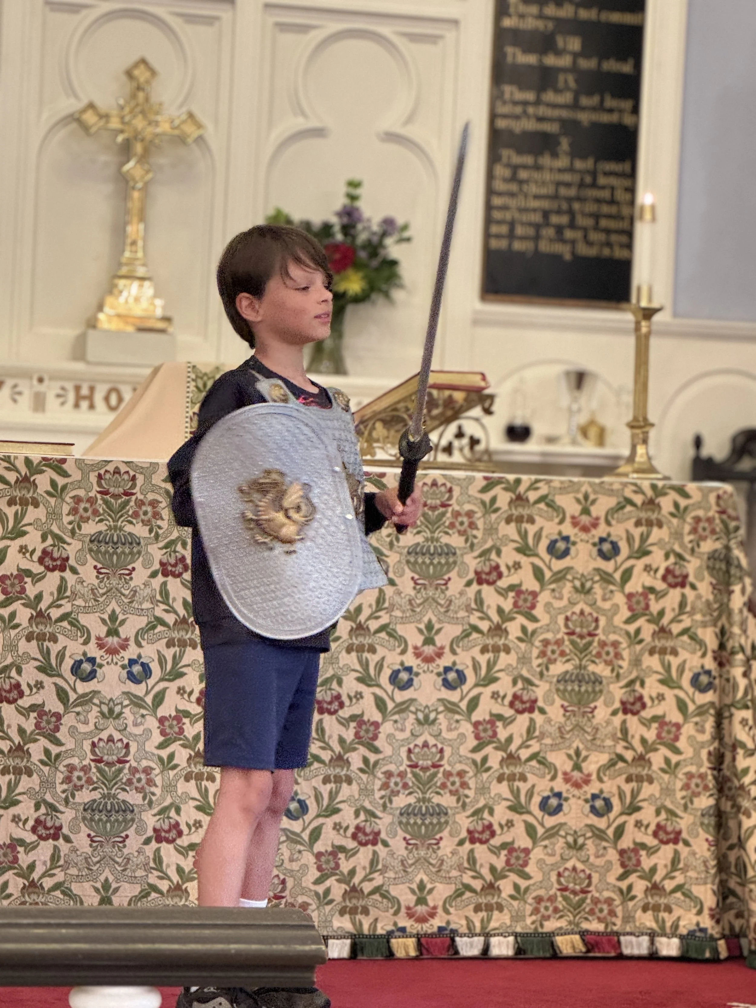Child dressed as a knight with sword and shield in a decorated room.