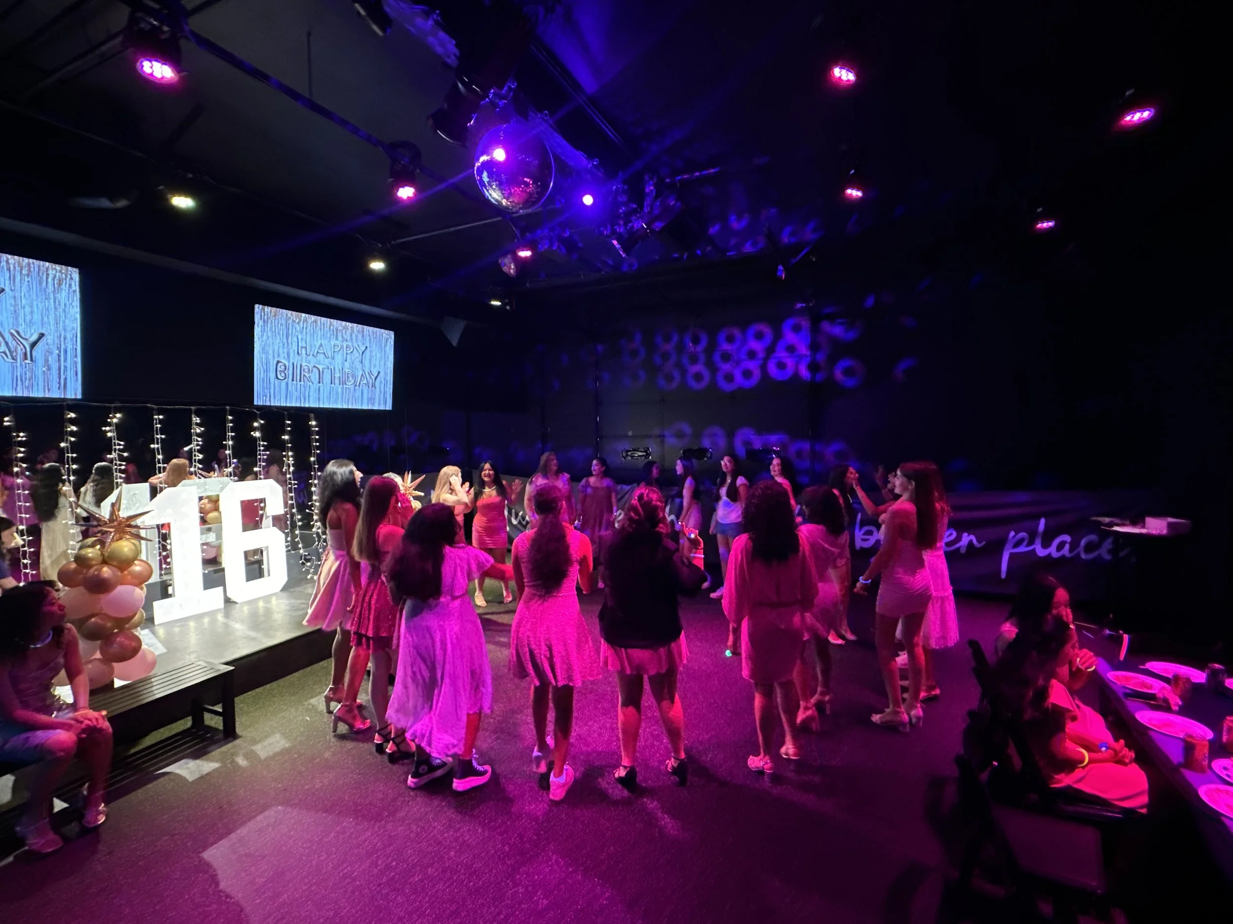 A group of girls celebrating a 16th birthday with a dance floor, balloons, and birthday decorations in a dark room with purple lighting.