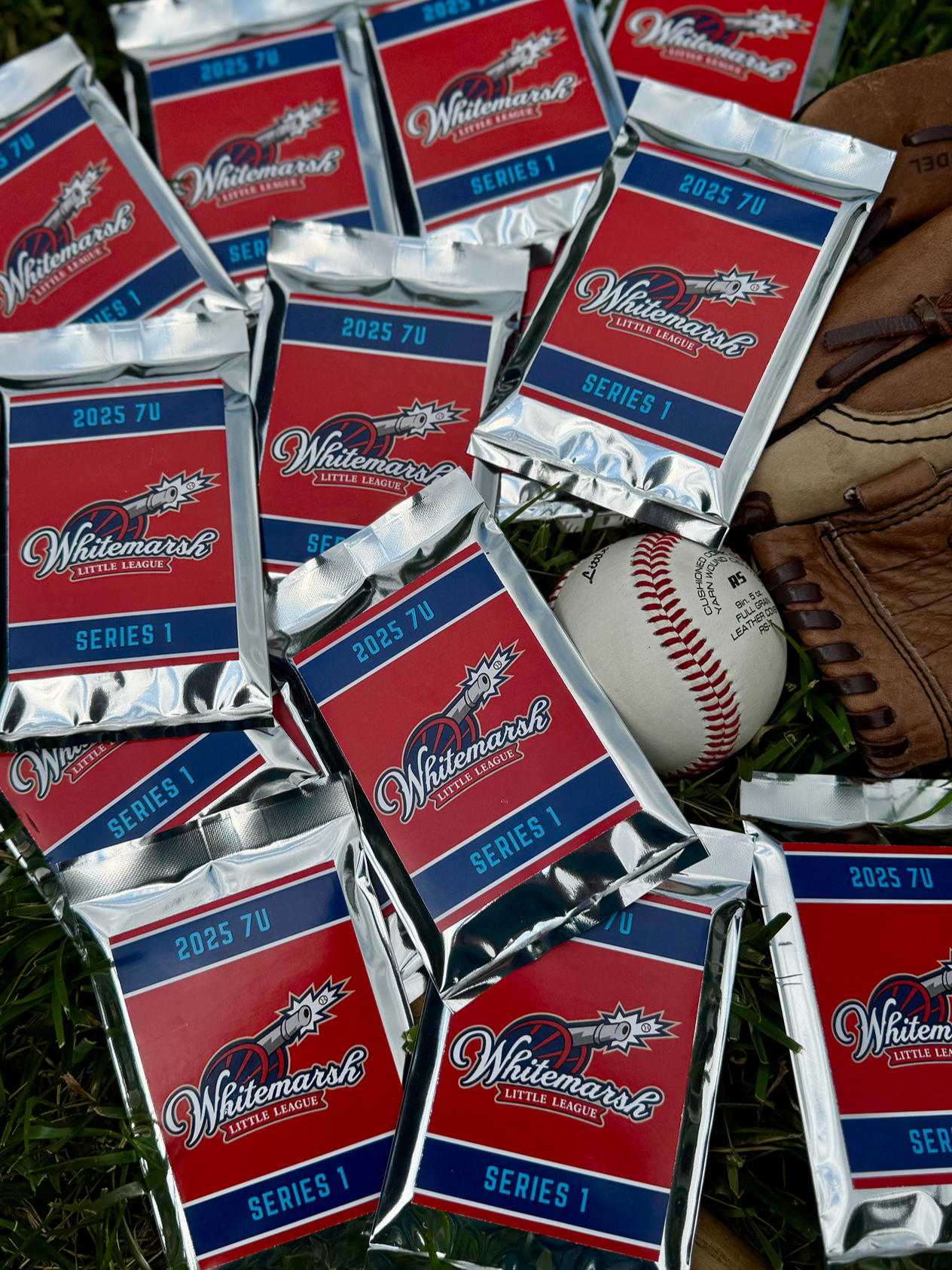 Multiple packages of Whitemarsh Little League baseball cards, a leather baseball glove, and a baseball on grass.