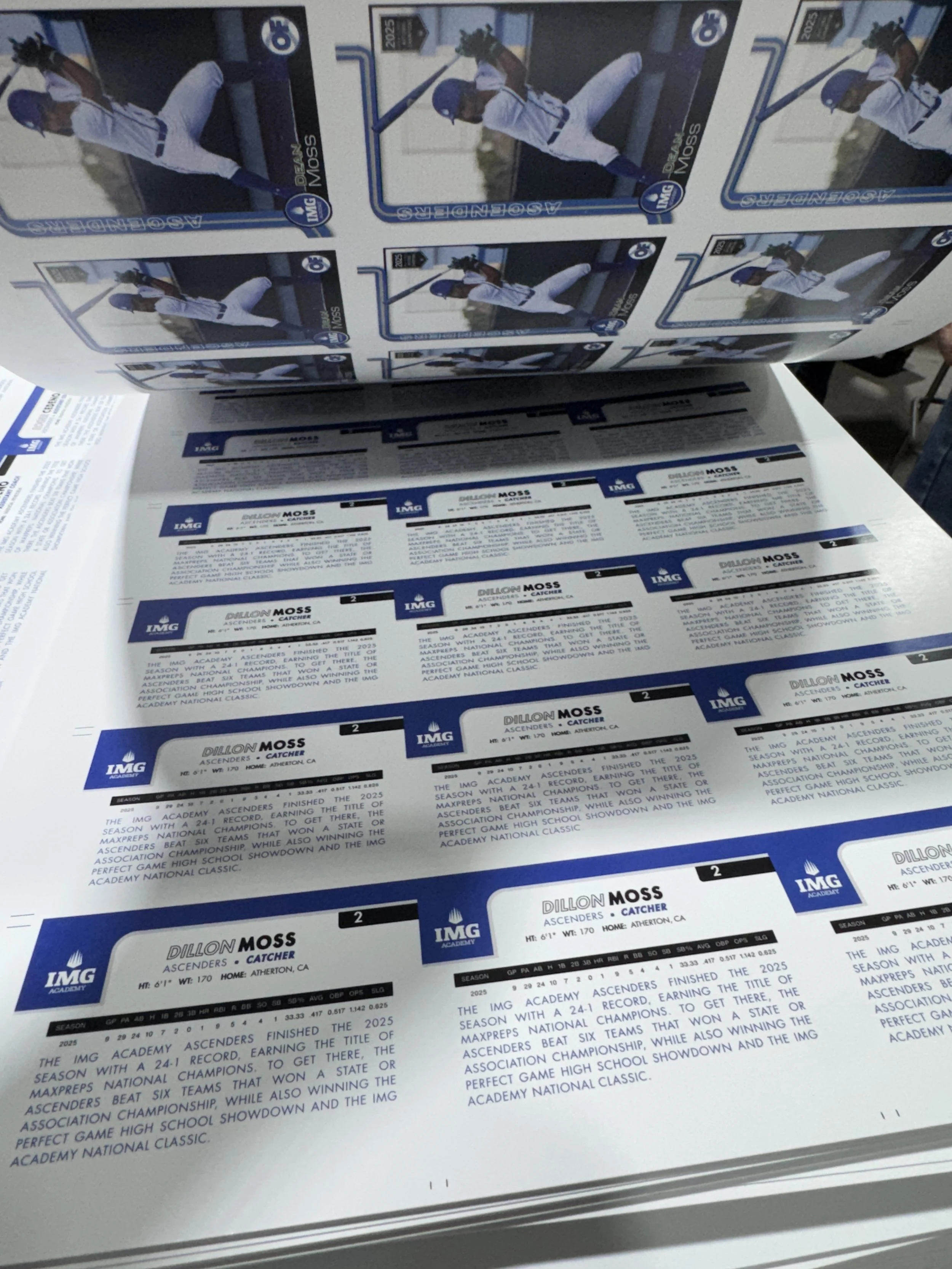 Stacked sheets of printed tickets and a poster with images of a baseball player in white uniform with blue helmet holding a bat.