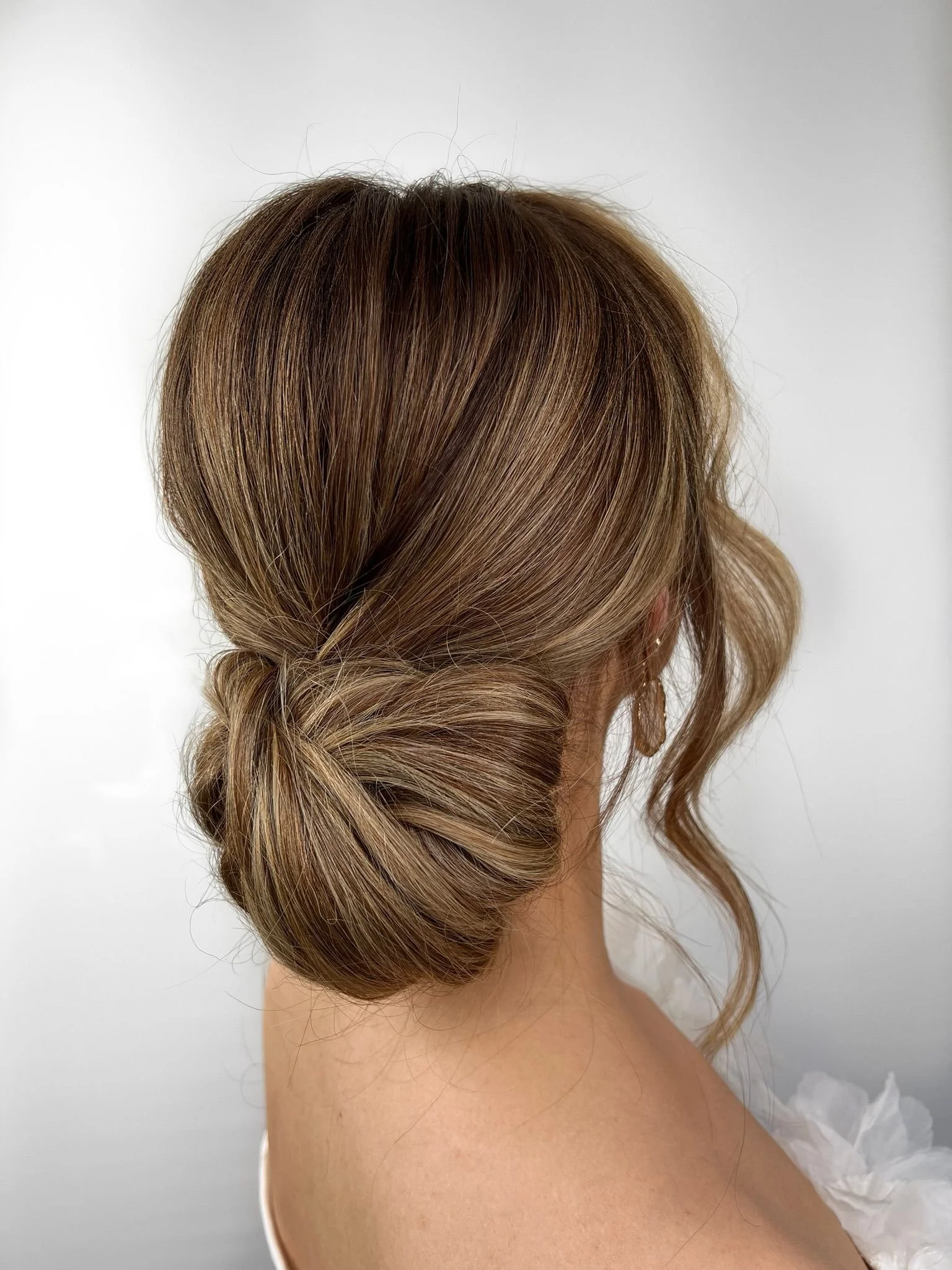 A woman with elegantly styled light brown hair in a low, twisted bun with soft waves.